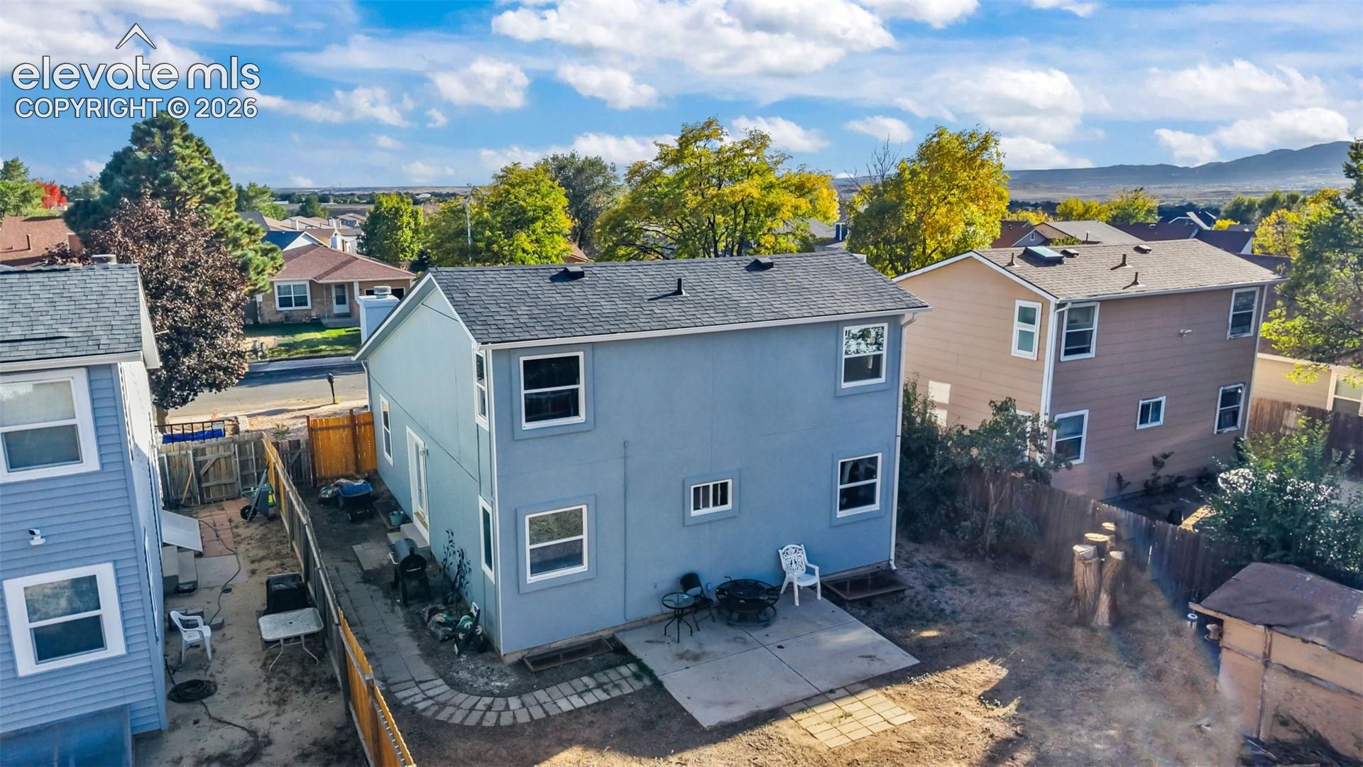 Two-story residence featuring light blue siding, a shingled roof, a concrete rear patio, and wood fencing