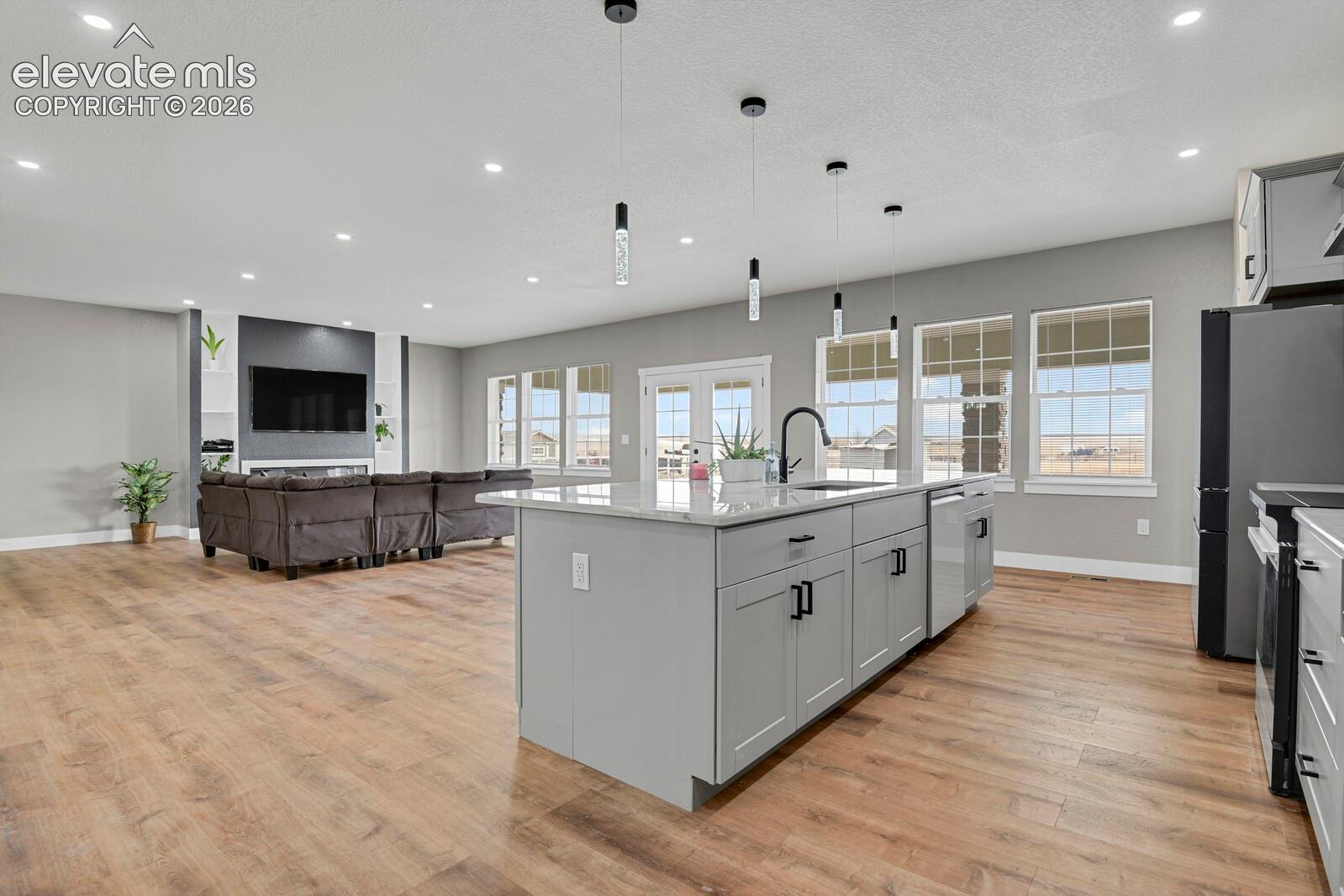 Open-concept living space with wood-finish flooring, a kitchen island with integrated sink, recessed lighting, and multiple large windows