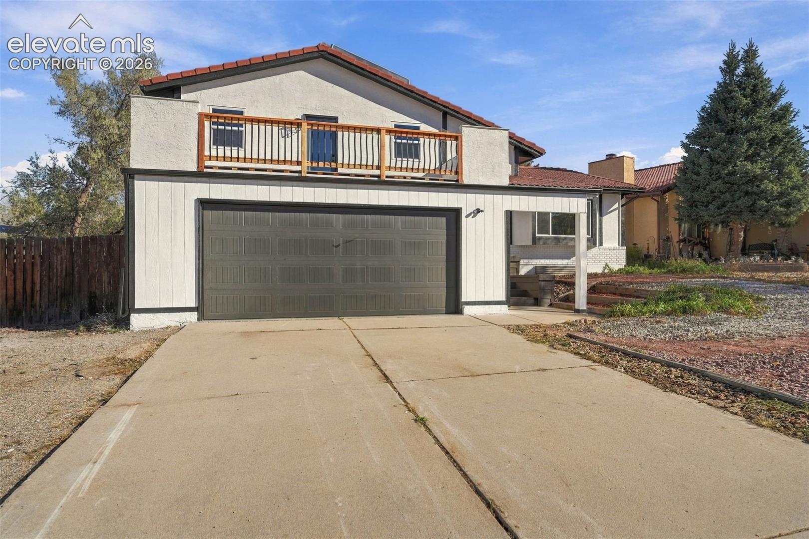 Two-story exterior featuring a concrete driveway, two-car garage, tiled roof, and a second-story wooden deck