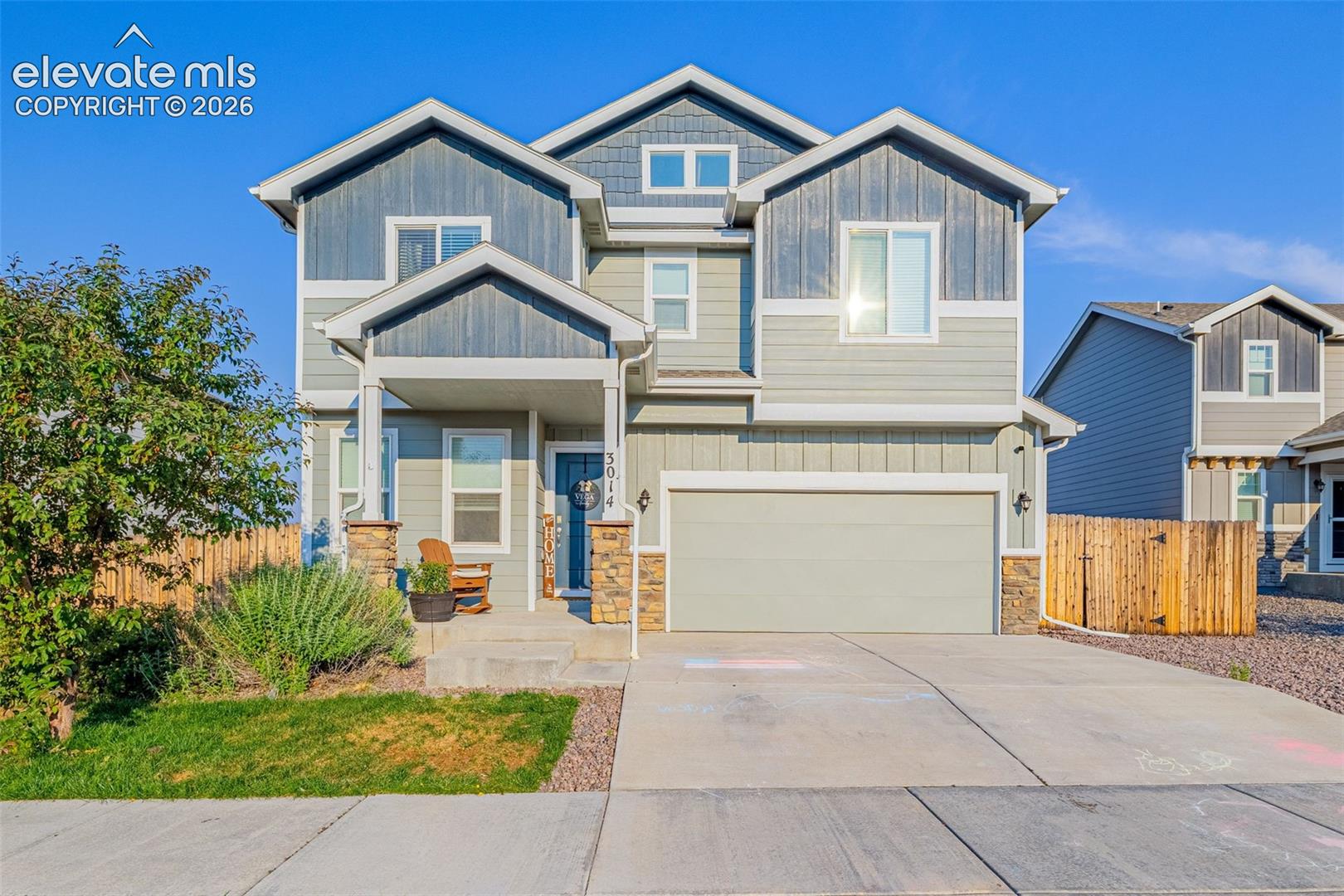 Two-story residence featuring a covered front porch with stone-clad columns, an attached garage, a paved driveway, and a partially fenced yard