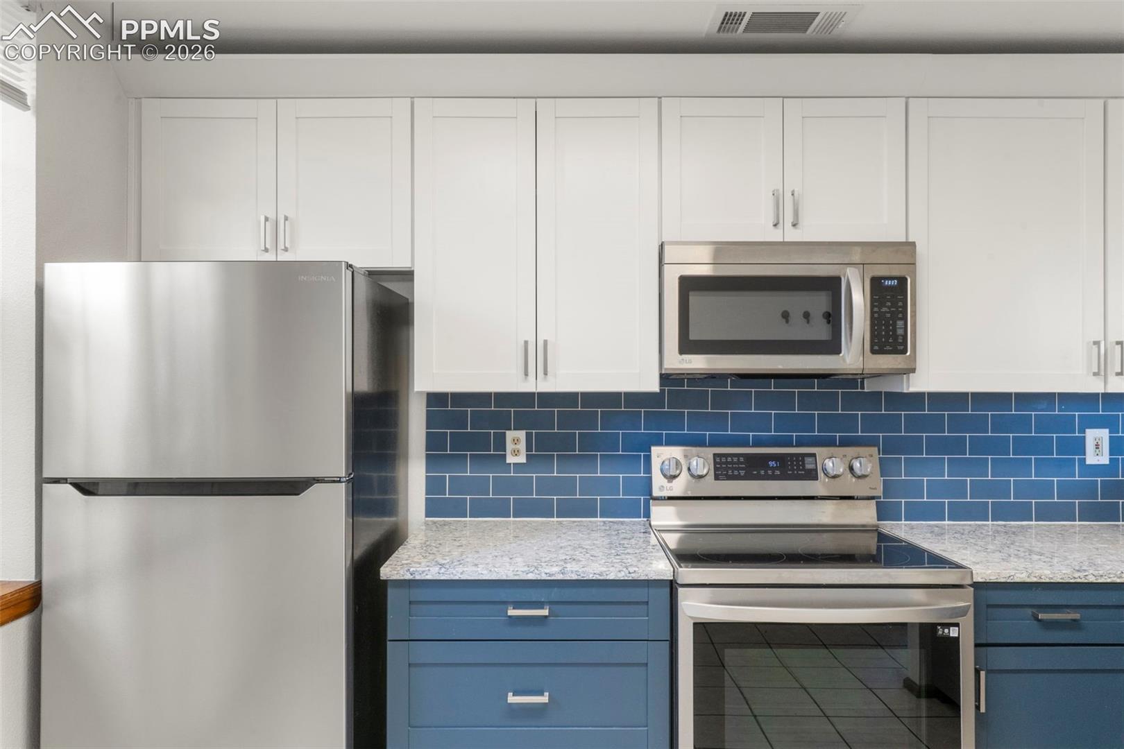Kitchen featuring stainless steel appliances, light stone countertops, decorative backsplash, and dual tone cabinets