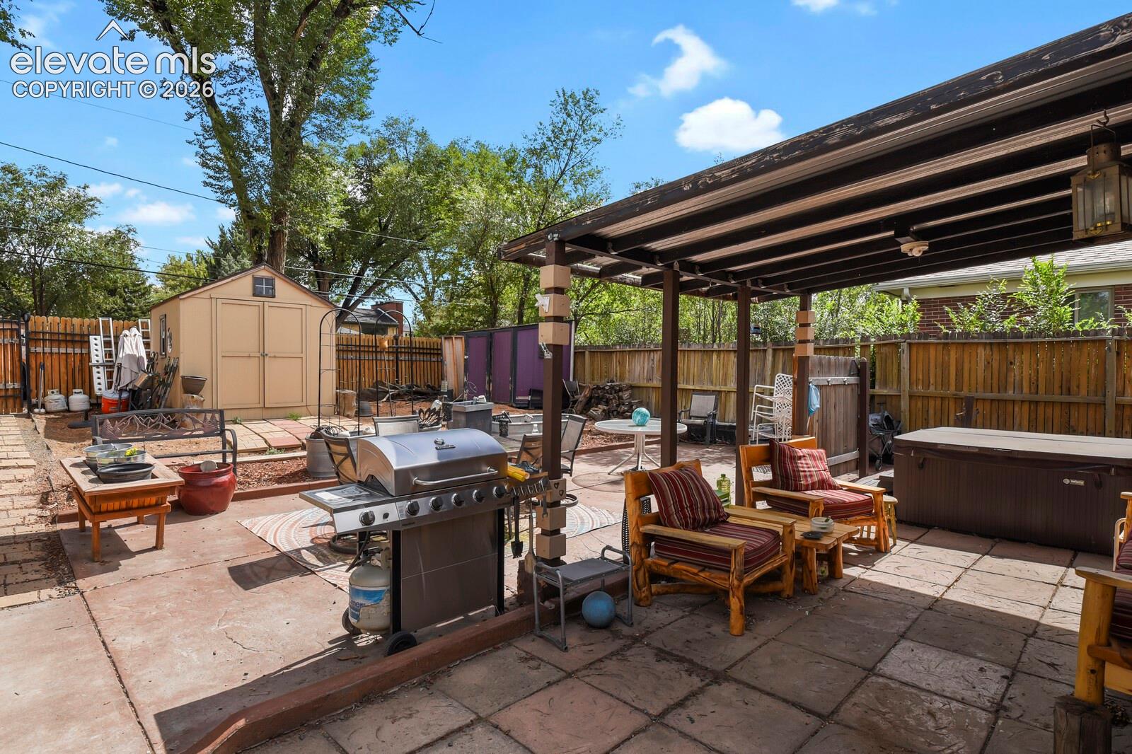 Expansive outdoor patio with a built-in pergola, stone paver and concrete surfaces, wood fencing, and a detached storage shed