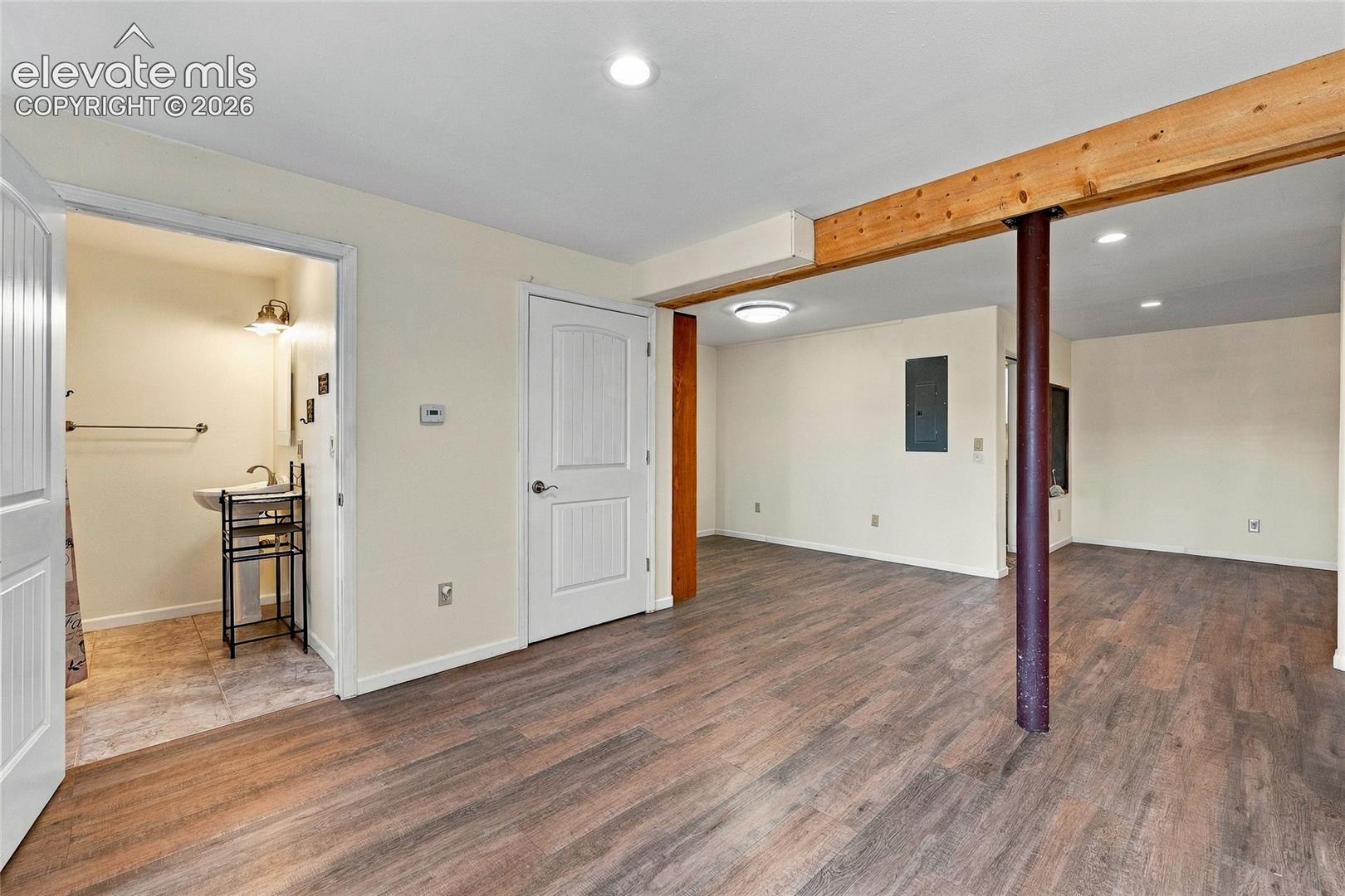 Open interior space featuring wood-finish flooring, exposed natural wood ceiling beam, recessed lighting, and a powder room with a pedestal sink