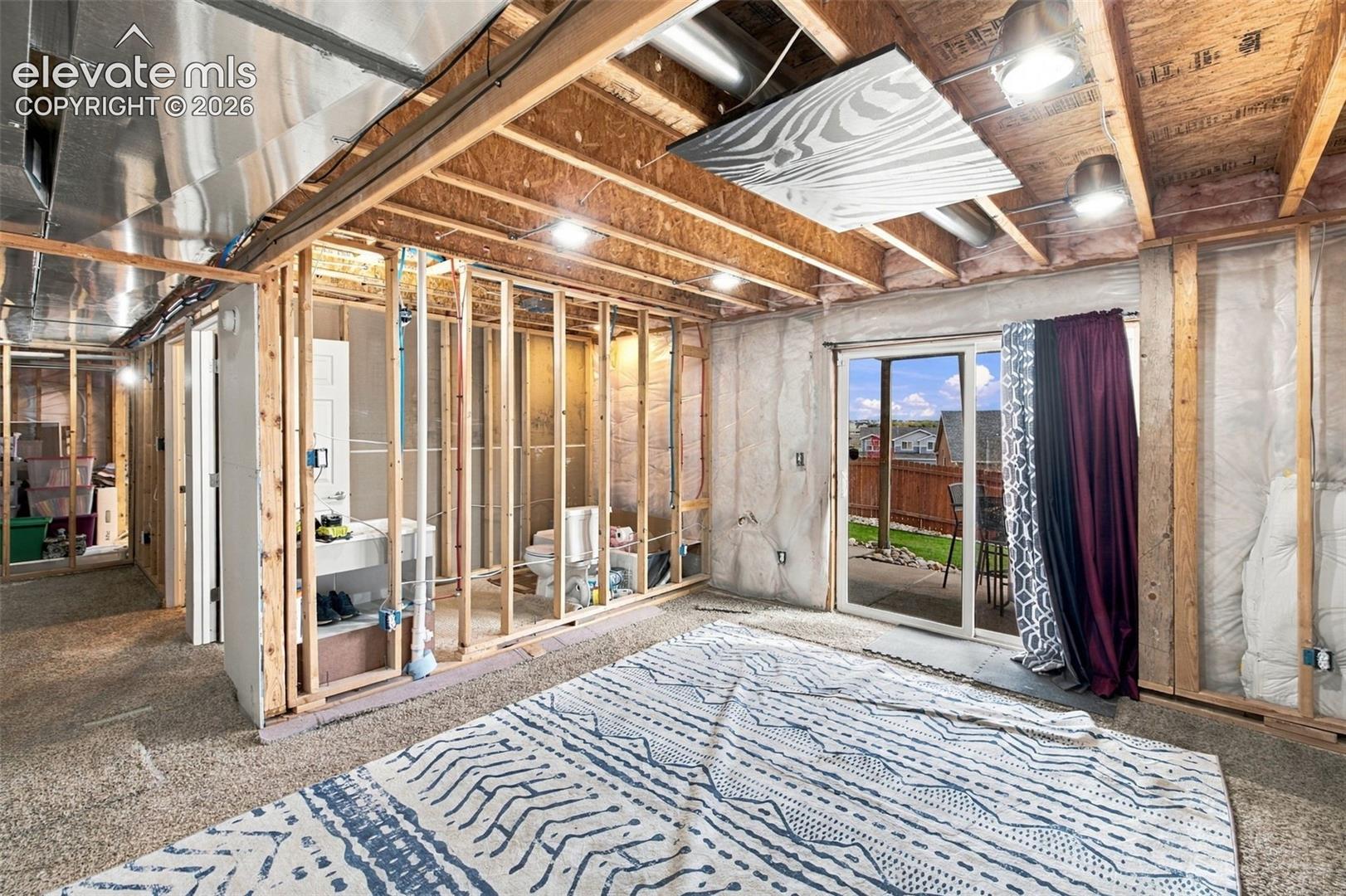 Unfinished lower level featuring exposed wood framing, insulating wall panels, recessed lighting, and a sliding glass door providing external access