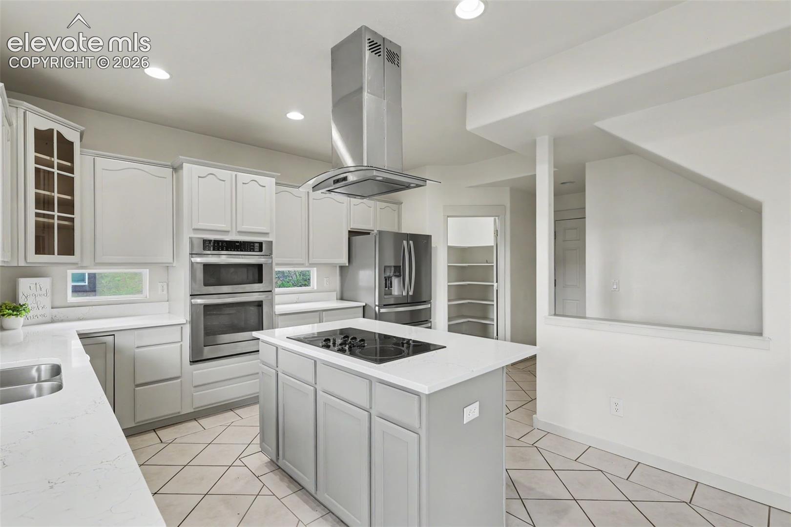 Modern kitchen featuring light gray cabinetry, stainless steel appliances, a center island with an integrated cooktop, and light-toned countertops