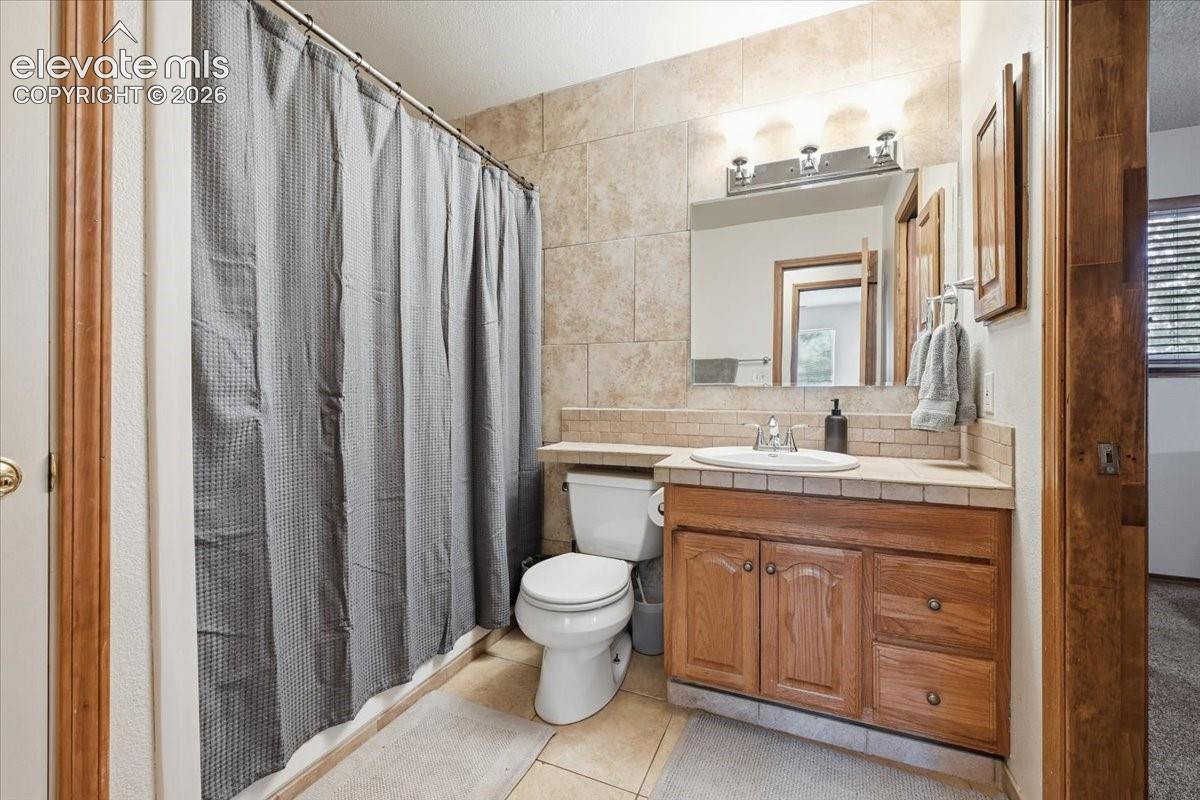 Tile flooring, tile shower surround, wood-finish vanity, integrated sink, and wall-mounted light fixture