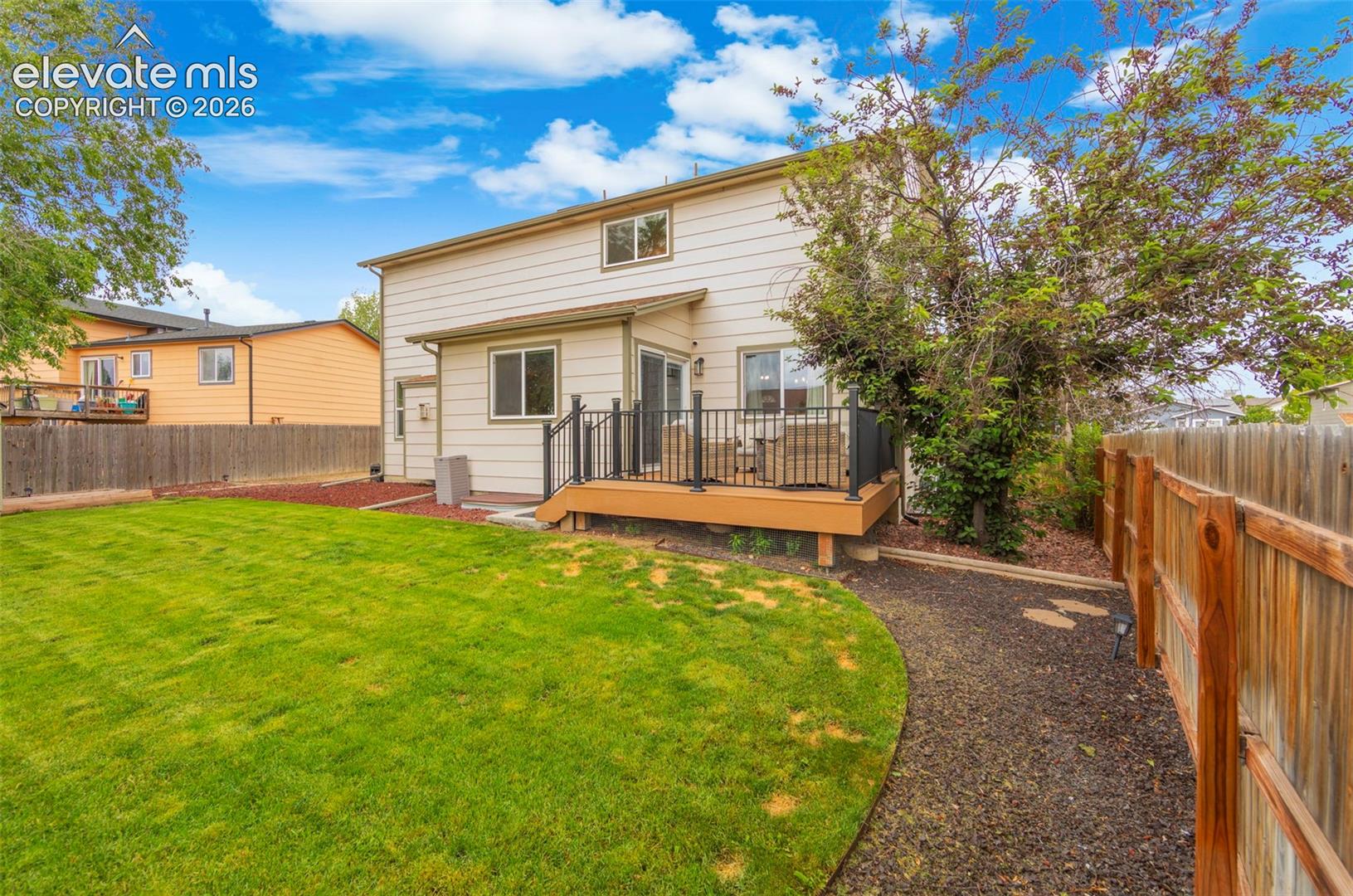 Expansive backyard featuring a manicured lawn, wood fencing, and a gravel pathway