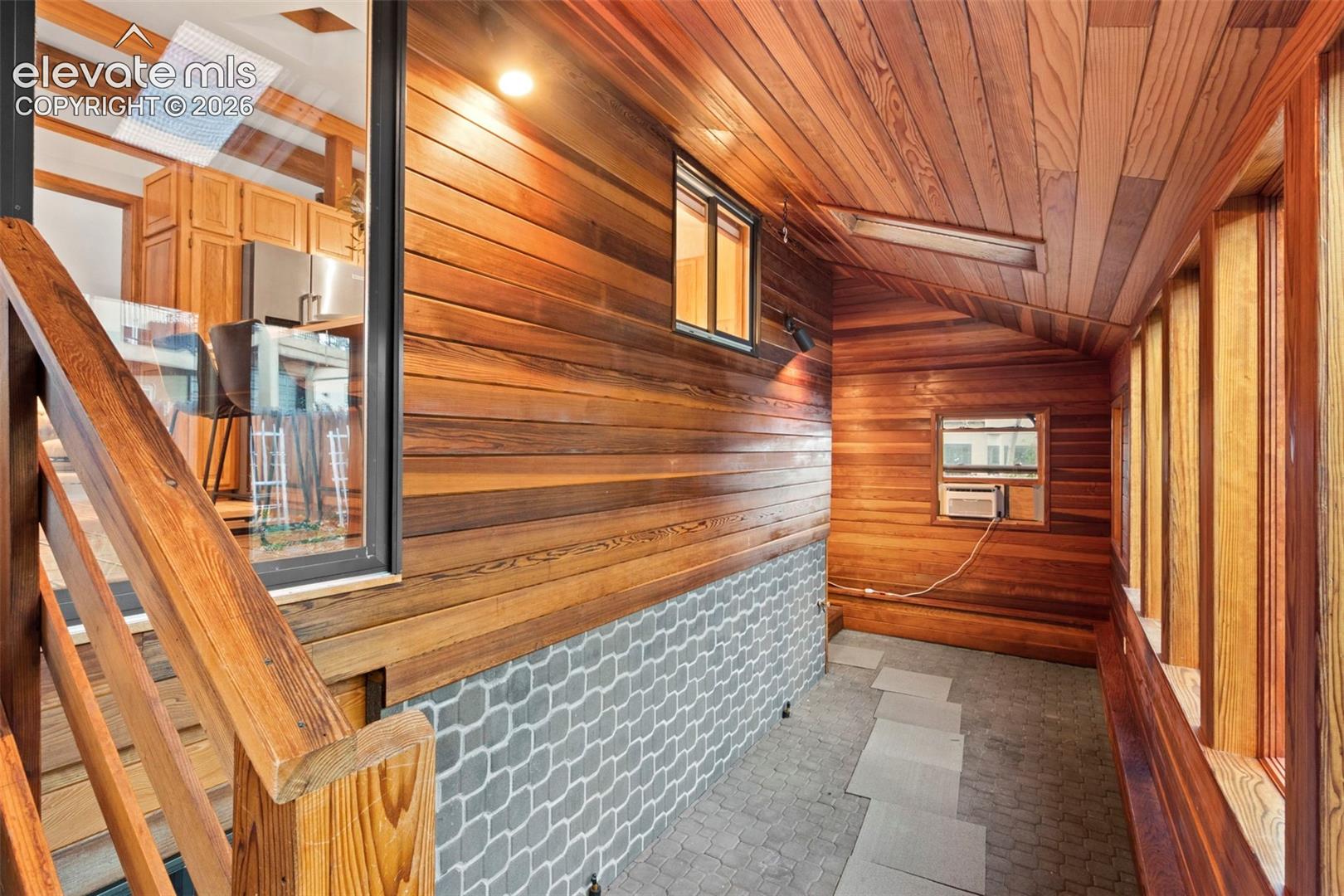 Enclosed space featuring natural wood-paneled walls and ceiling, stone-patterned accent wall, skylights, and stone-tiled flooring