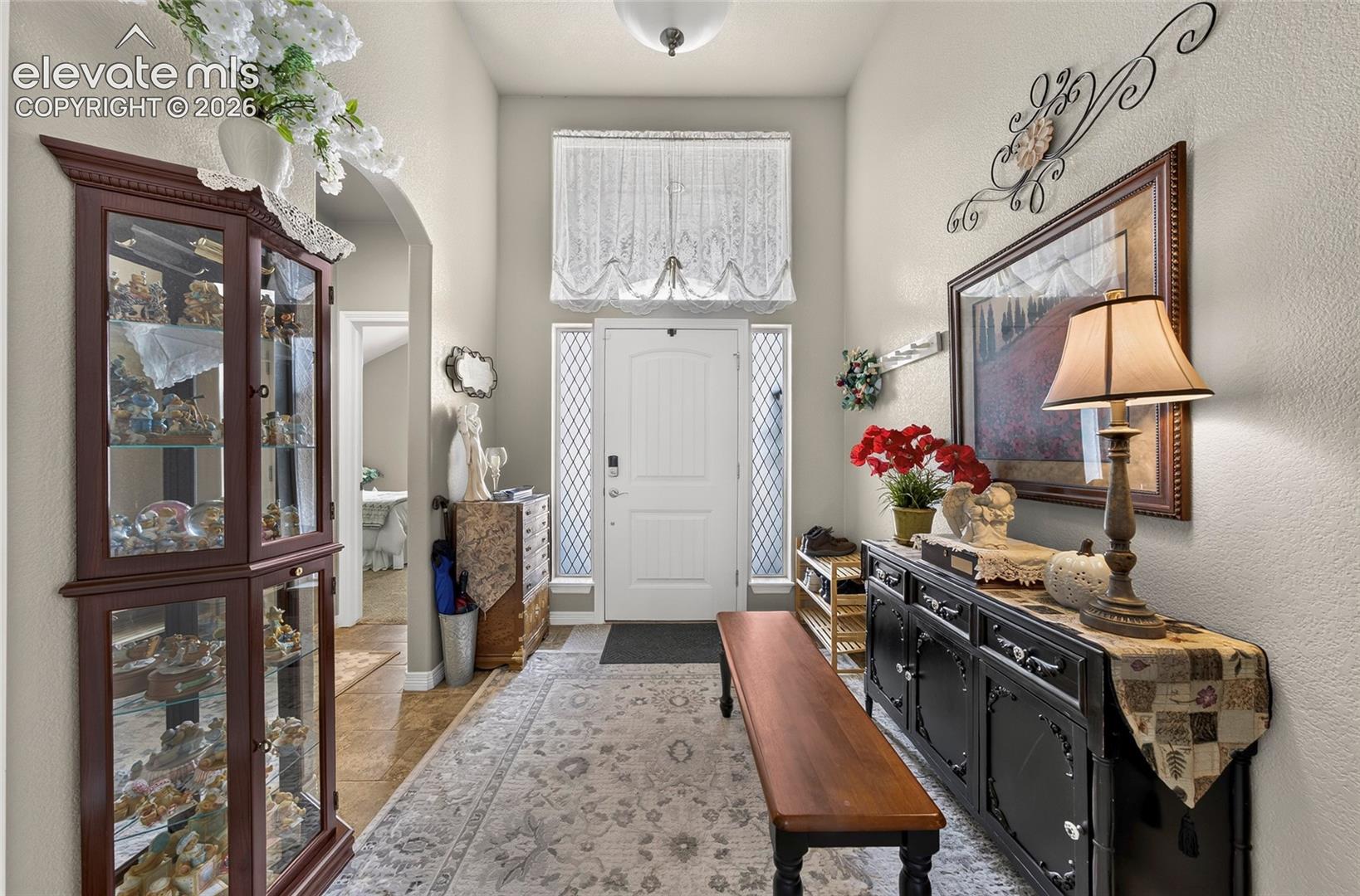 Foyer featuring high ceilings, a single-panel front door with sidelights, a decorative transom window, and tile flooring