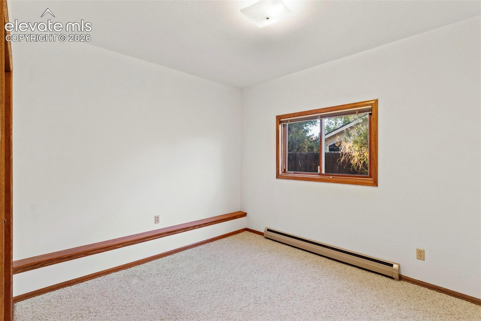 Neutral-toned carpeted room featuring a built-in wood-trim ledge, a sliding window with wood casing, and a square flush-mount ceiling fixture