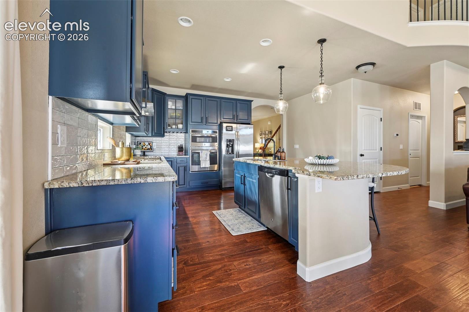 Kitchen featuring navy blue cabinetry, stone countertops, stainless steel appliances, wood-finish flooring, and dual glass pendant light fixtures