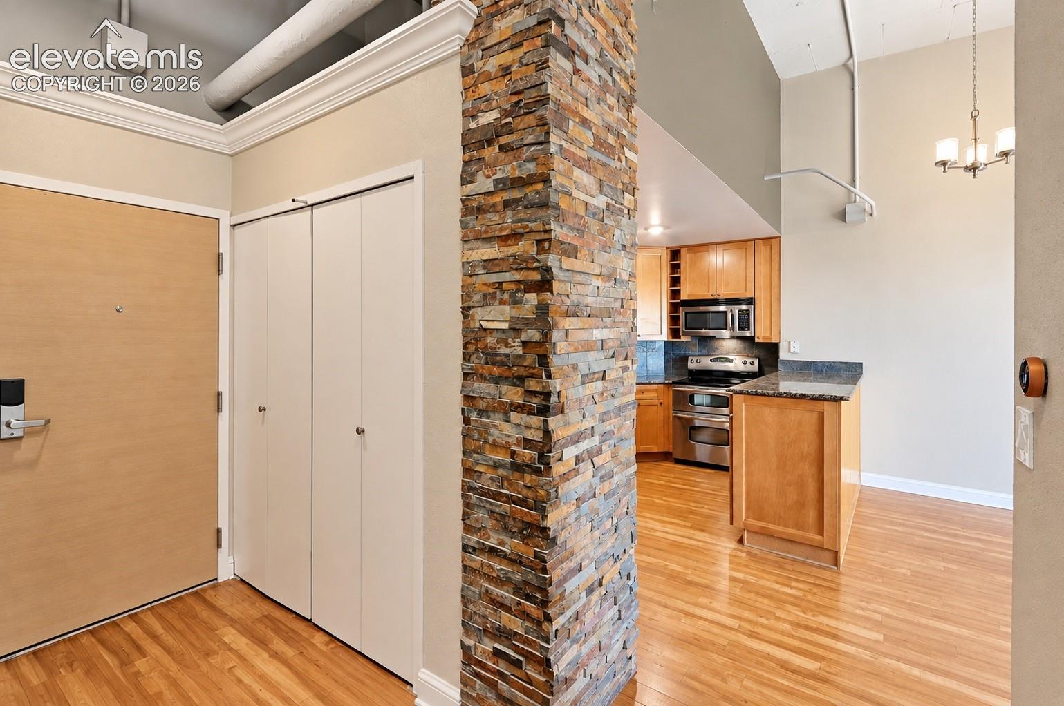 Stone-clad architectural column, wood-finish flooring, kitchen with stainless steel appliances, wood cabinetry, and a built-in kitchen island
