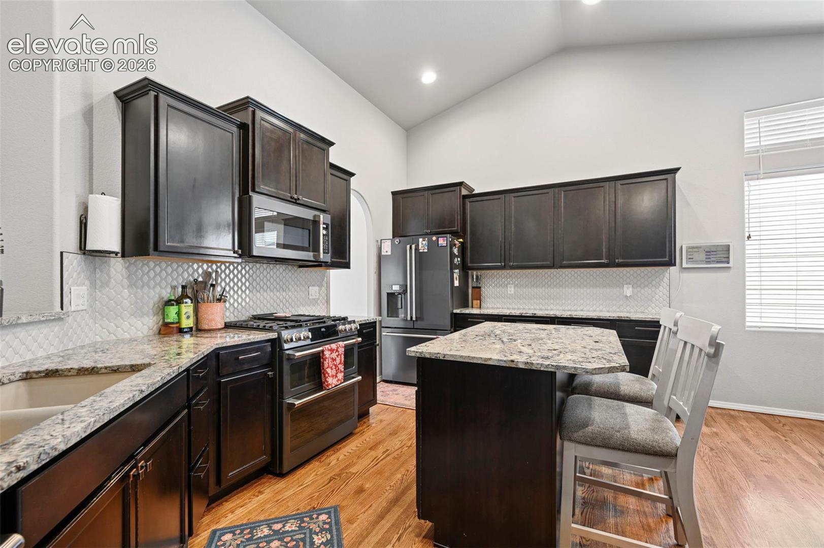 Kitchen featuring vaulted ceilings, dark-finish cabinetry, granite countertops, a center island with seating, and wood-finish flooring