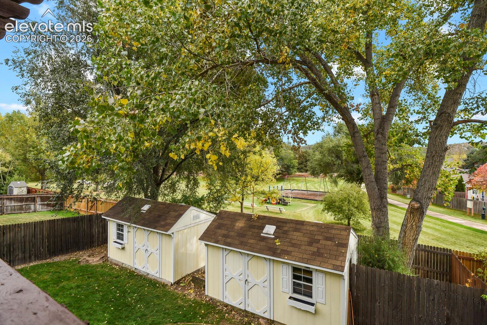 Rear yard featuring two storage structures, a fenced perimeter, and mature trees