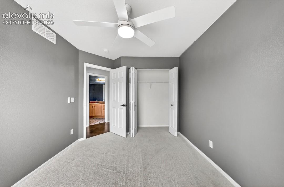 Neutral-toned interior featuring wall-to-wall carpeting, grey wall finish, white ceiling fan with integrated lighting, and a dual-door closet