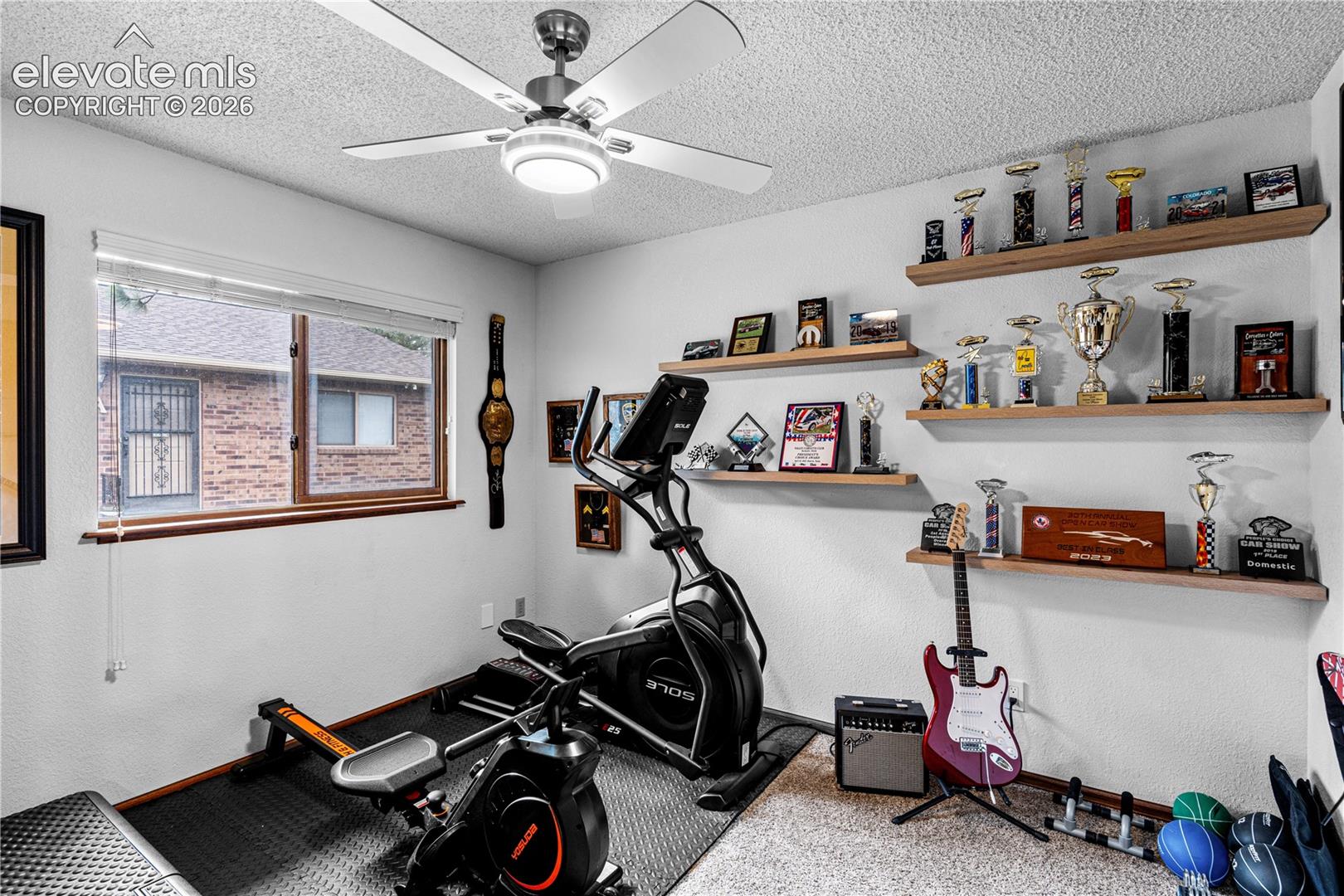 Room featuring wall-mounted floating wood shelving, a ceiling fan with integrated lighting, and a large horizontal window