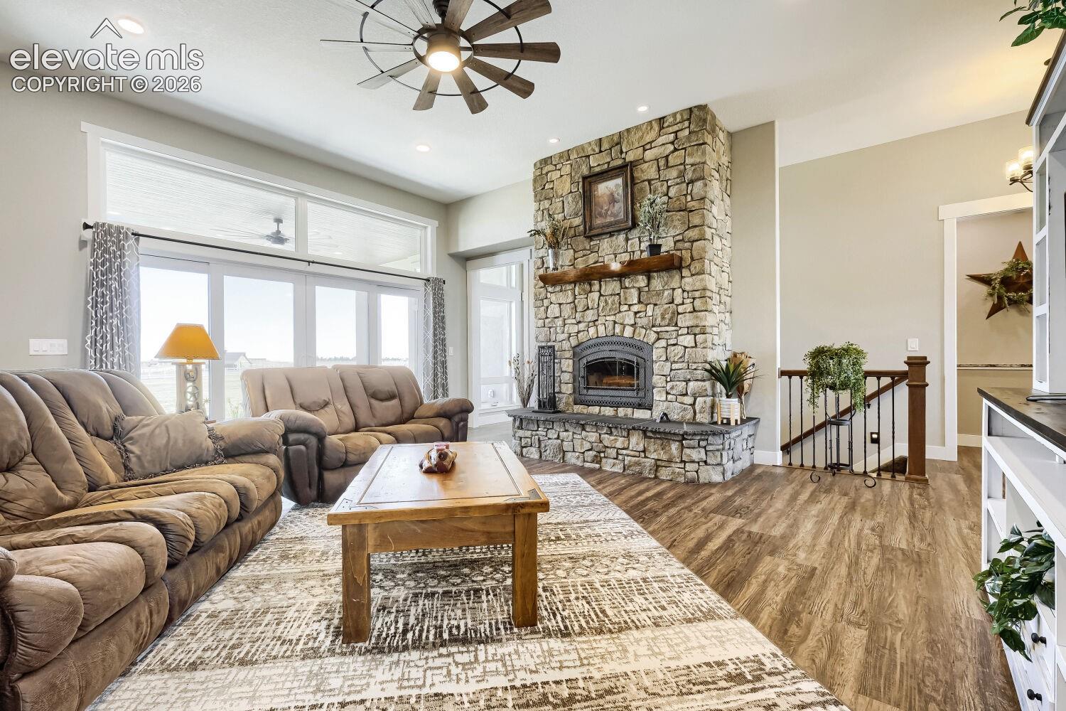 Spacious living area featuring a stone-clad fireplace with a wood mantle, wood-finish flooring, and large windows