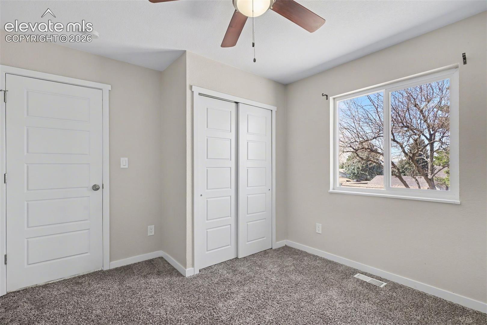 Neutral-toned interior featuring wall-to-wall carpeting, a sliding-door closet, a single-panel interior door, and a ceiling fan with integrated lighting