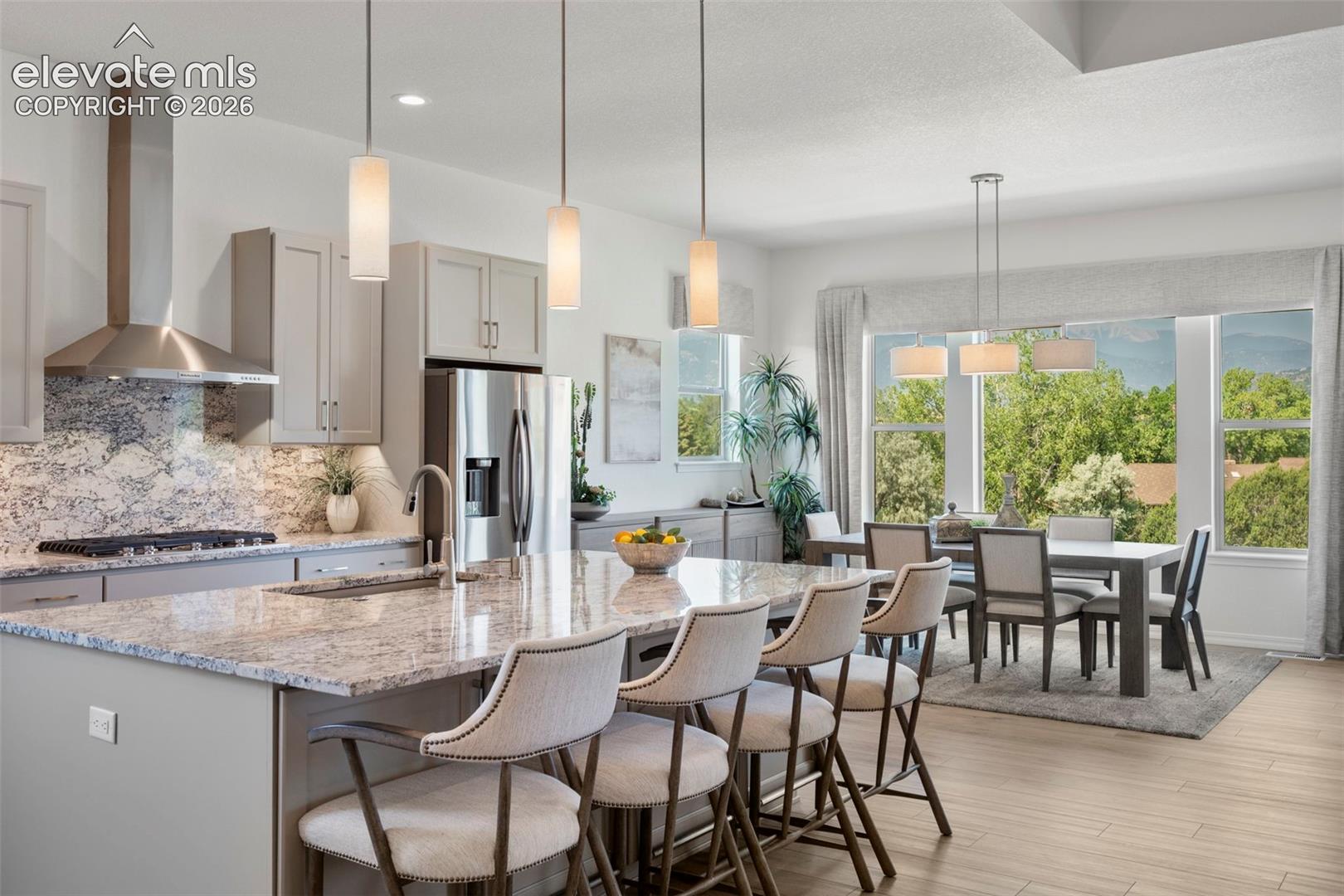 Kitchen island with integrated sink, stainless steel appliances, stone countertops, light wood-finish flooring, and expansive windows