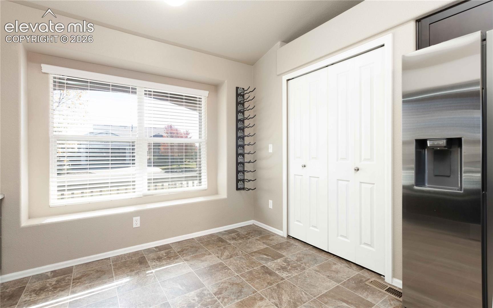 Recessed window nook featuring a multi-pane window, tile flooring, stainless steel refrigerator, and wall-mounted storage rack