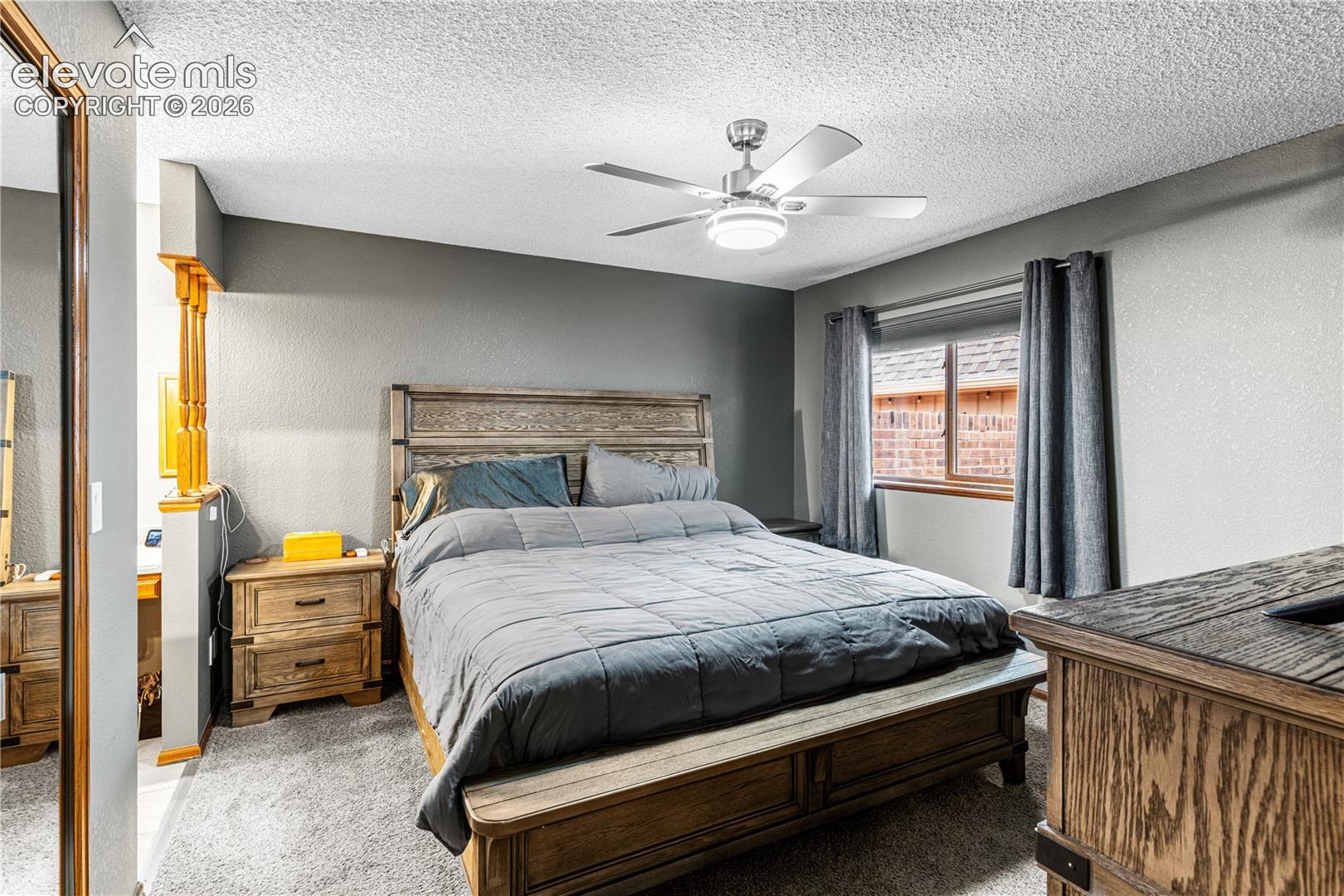 Neutral wall tones, carpeted flooring, ceiling-mounted light fixture with fan, and partial-height wall partition with wooden balusters