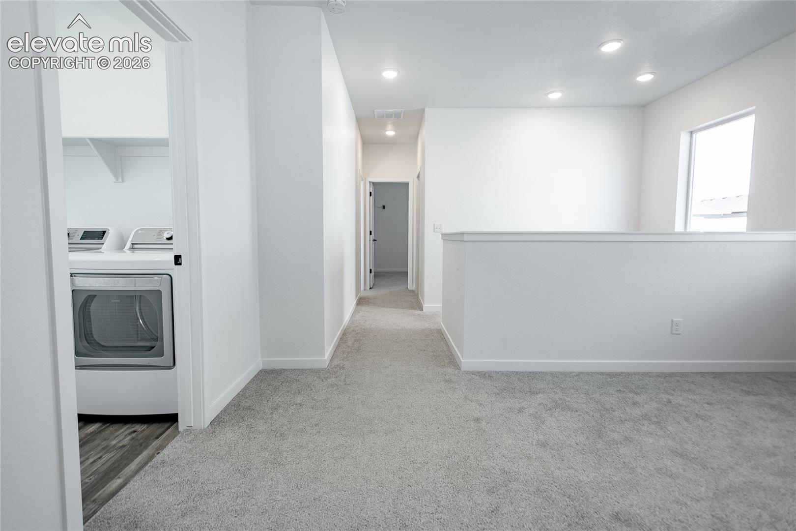 Neutral-toned carpeting, recessed ceiling lighting, and a dedicated laundry area featuring built-in shelving