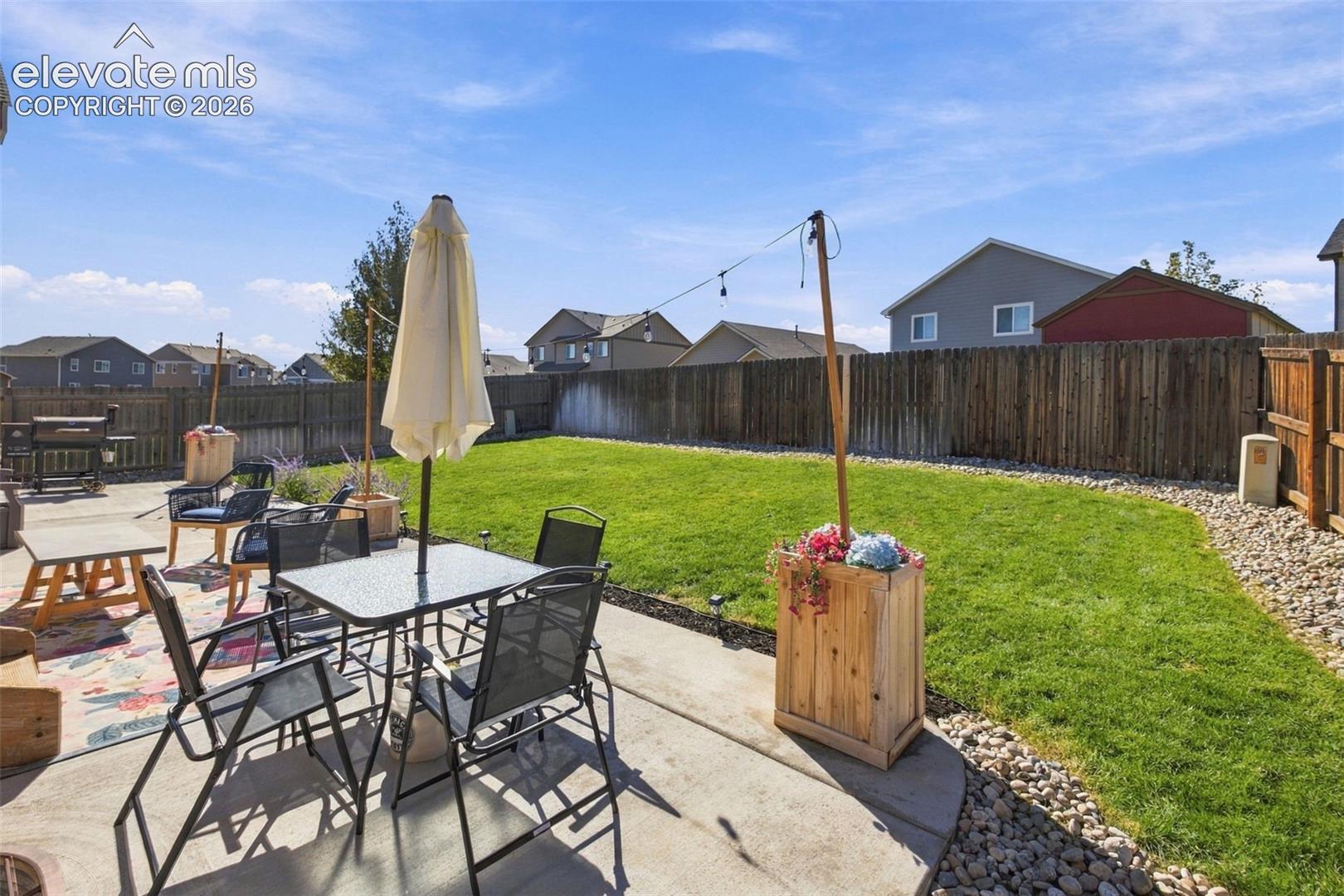 Concrete patio, fenced backyard, and river rock landscape borders