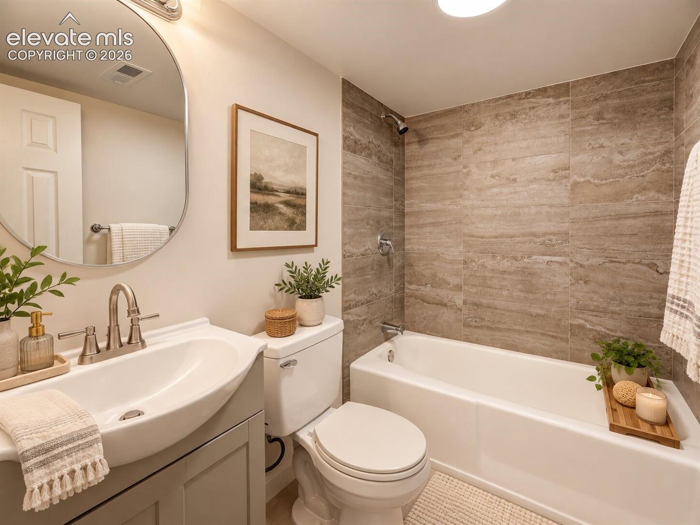 Bathroom featuring a vanity with an integrated porcelain sink, wide-profile oval mirror, tub-and-shower combination with floor-to-ceiling stone-look tiling, and brushed-nickel hardware. AI-Enhanced – furniture/decor digitally added