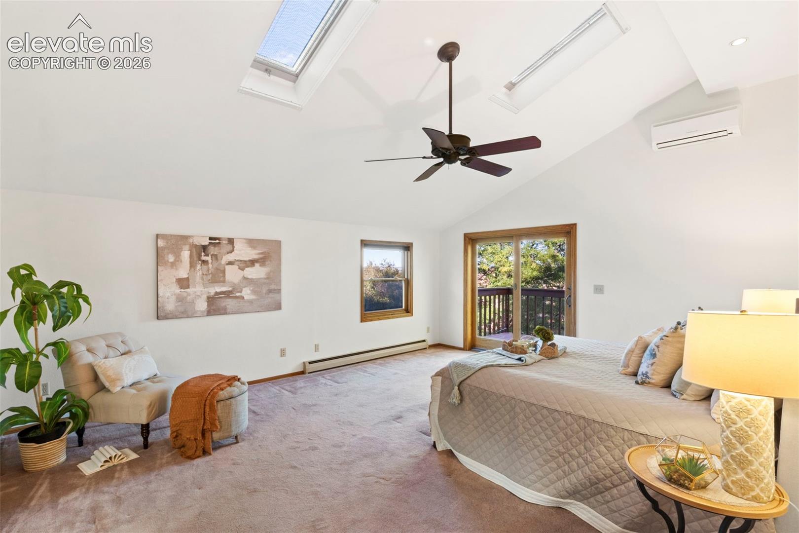 Vaulted ceiling featuring dual skylights, ceiling fan, wall-mounted climate control unit, and sliding glass door access to a balcony