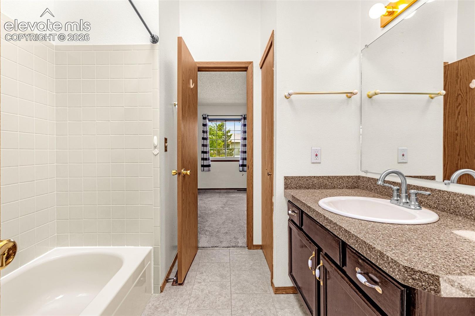 Bathroom featuring a built-in bathtub with white tile surround, a dark wood-finish vanity, a surface-mount sink, and a framed mirror