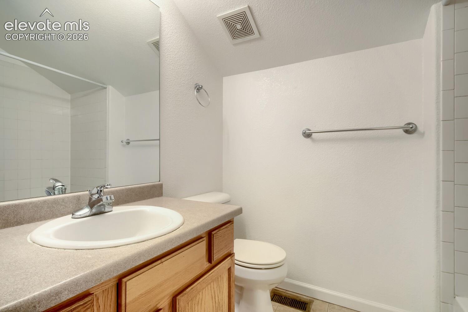 Bathroom featuring a wood-finish vanity with a neutral solid-surface countertop, an integrated oval sink, and a large wall-mounted mirror