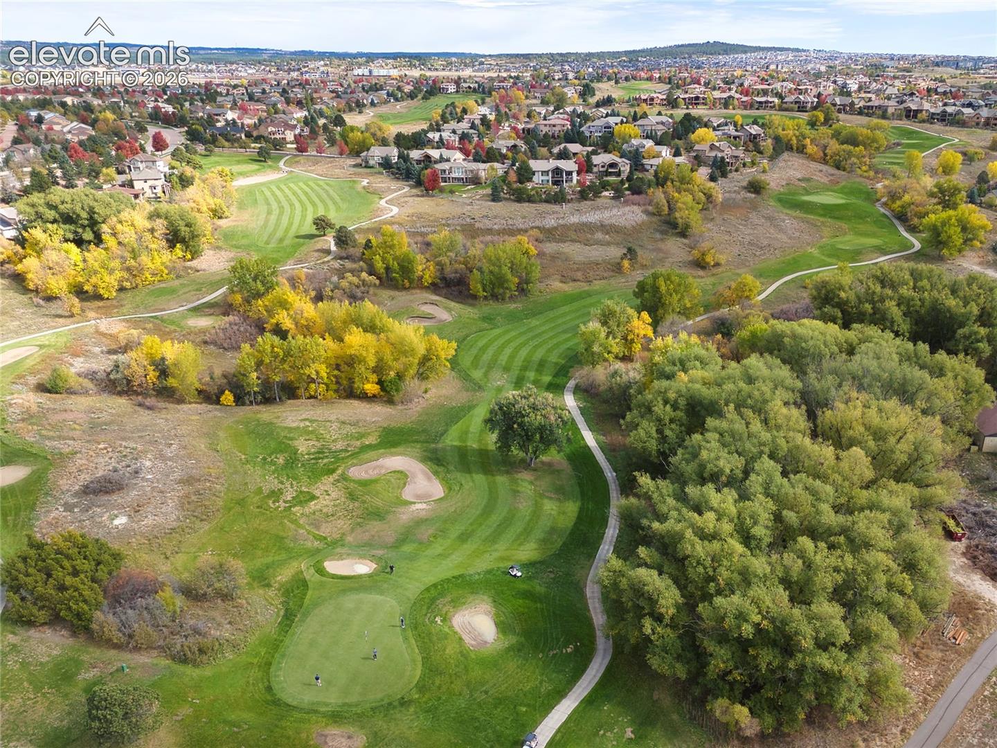 Aerial perspective featuring a manicured golf course, sand traps, paved cart paths, and mature deciduous trees