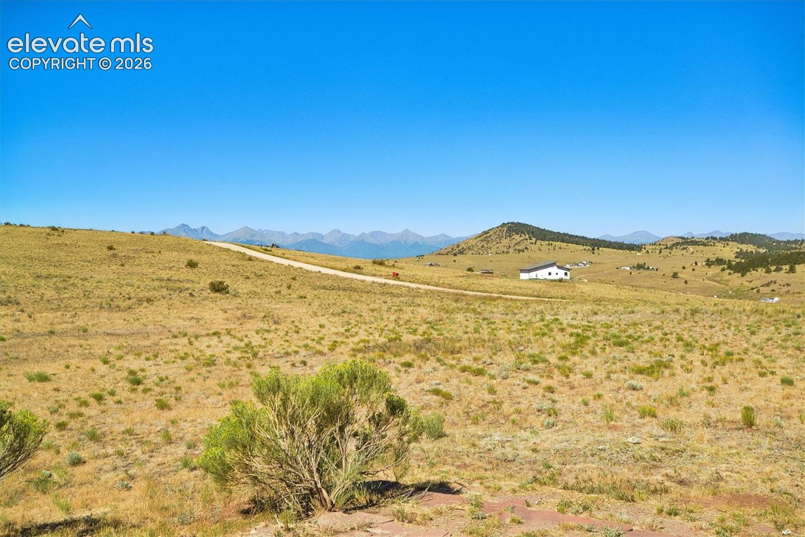 Expansive open terrain with a dirt road, distant mountains, and a white residence with a dark roof
