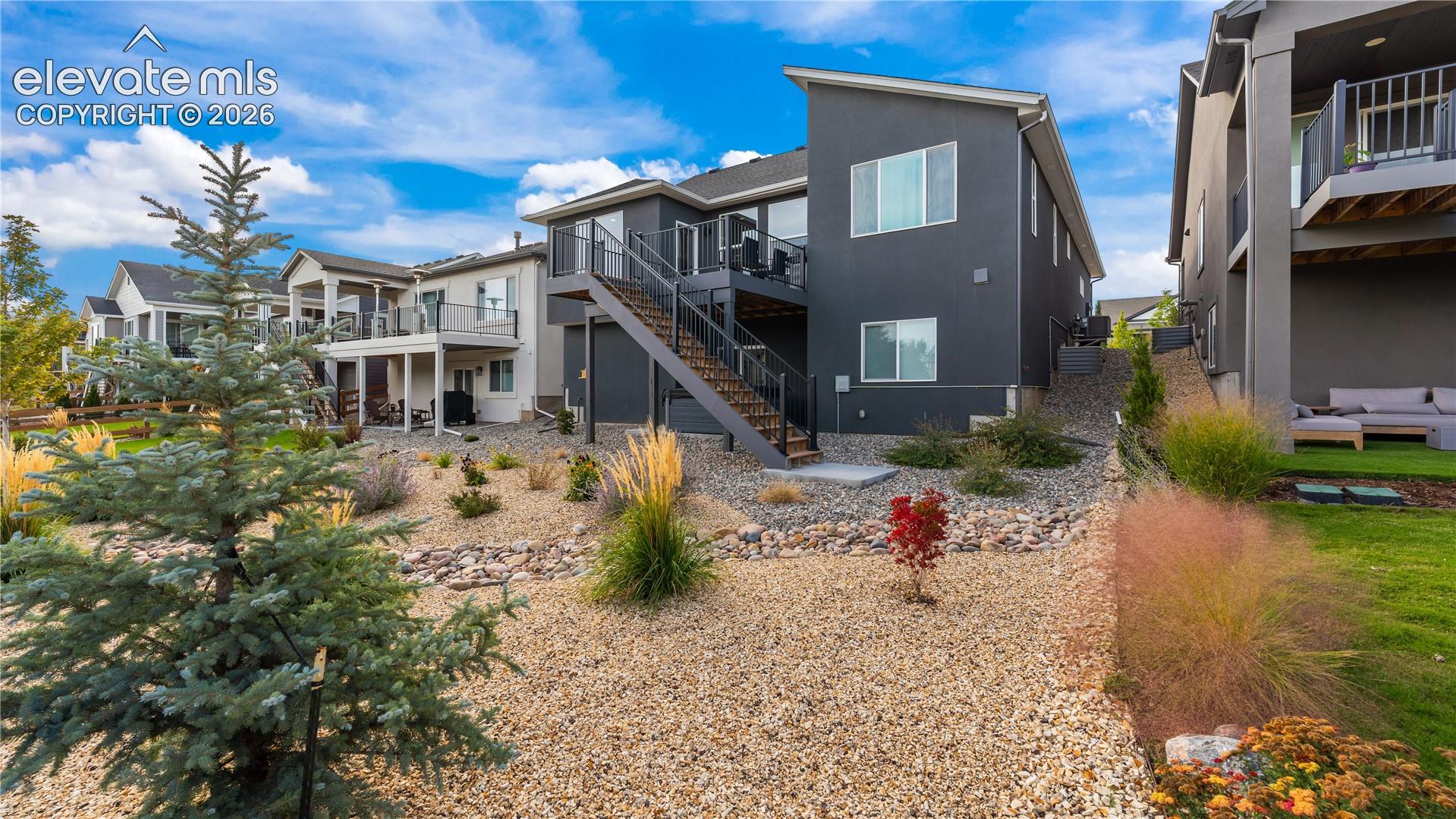 Contemporary multi-level exterior featuring dark-toned siding, elevated rear deck with metal railing, exterior staircase, and low-maintenance rock landscaping