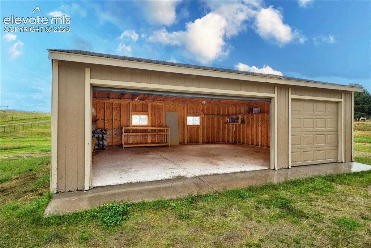 Detached garage featuring vertical siding, a concrete floor, built-in wooden shelving, and two windows