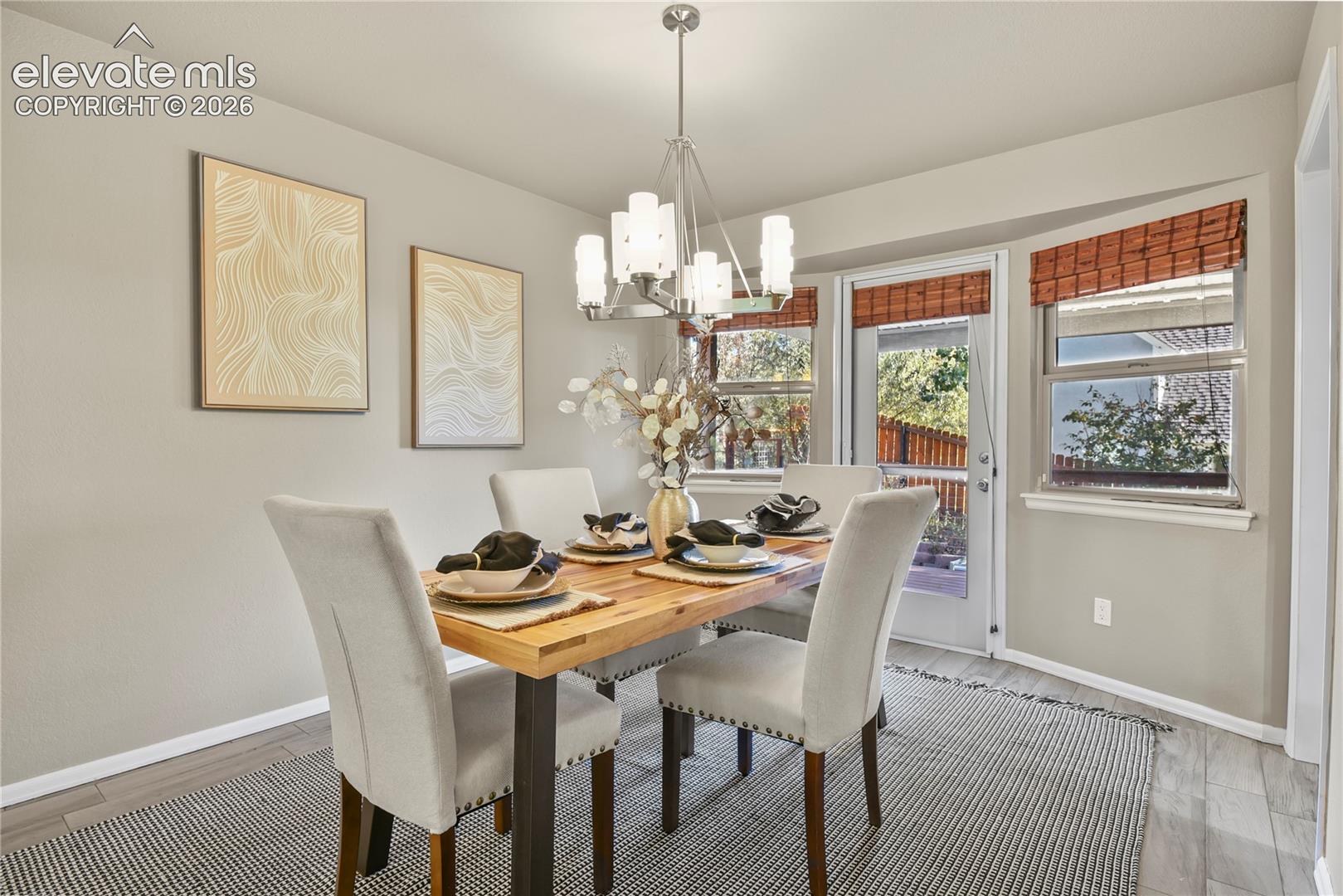 Dining area featuring wood-finish tile flooring, a multi-arm metallic chandelier, bay windows with integrated door access, and neutral wall tones