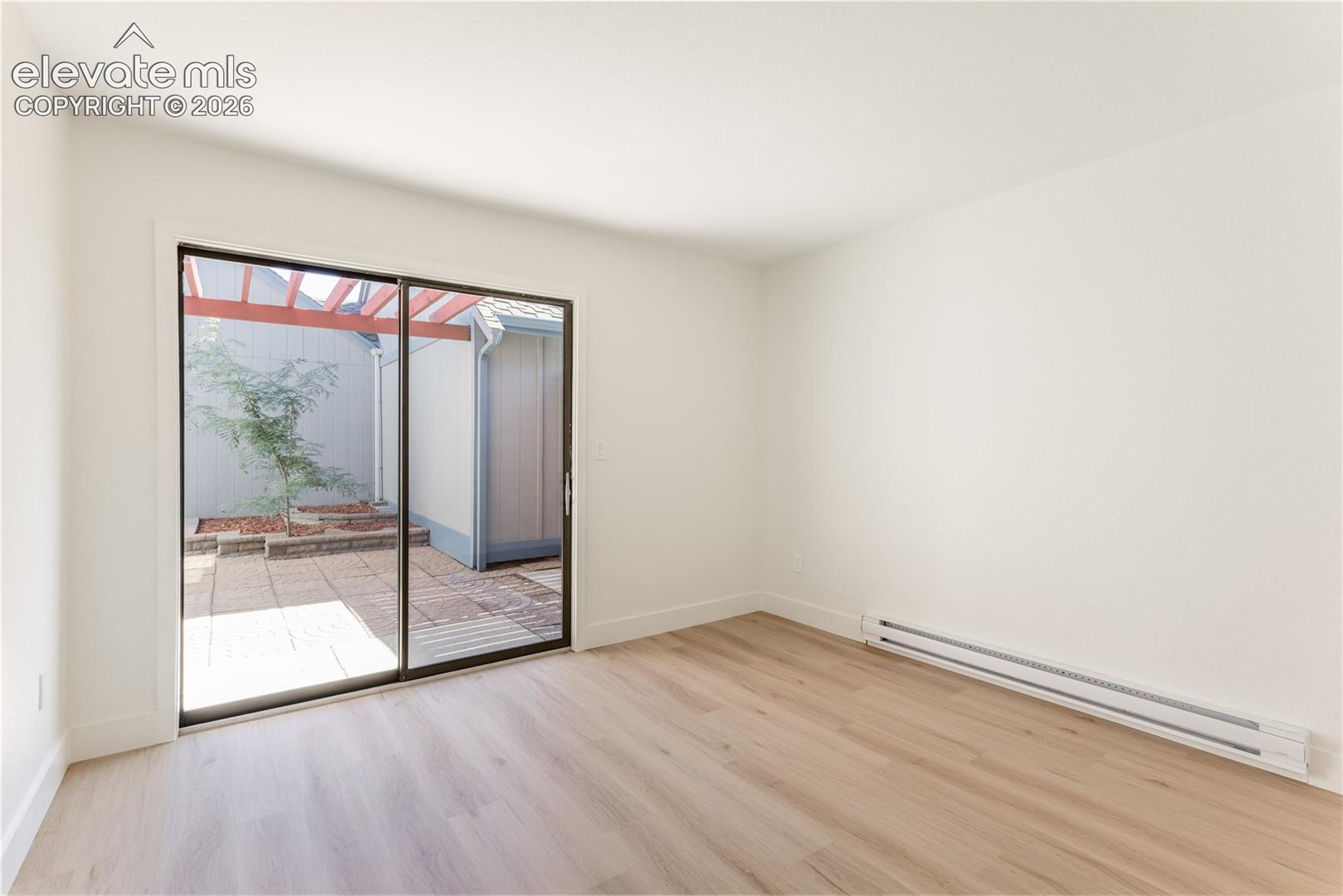 Interior space featuring wood-finish flooring, sliding glass door, and a paved outdoor patio area with a wooden pergola