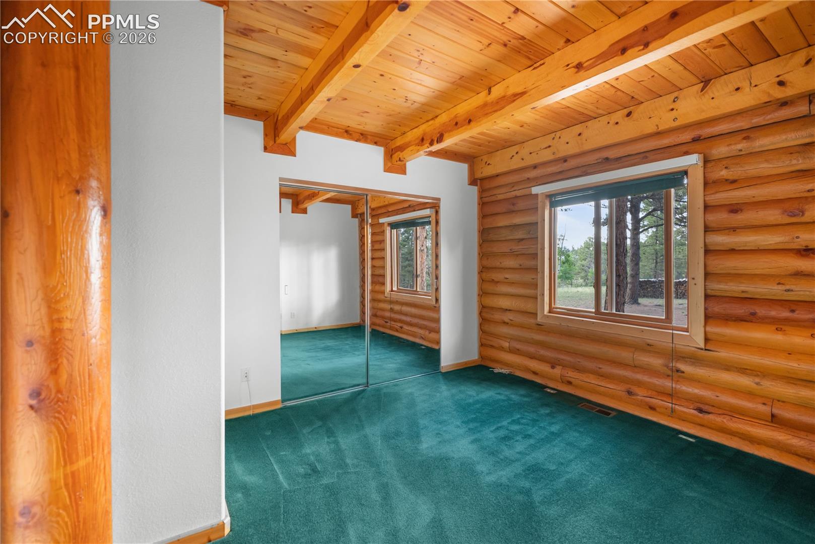 Empty room with rustic walls, a wooden ceiling with exposed beams, and carpet floors