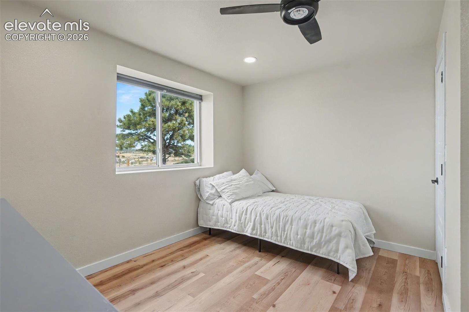 Room featuring wood-finish flooring, recessed lighting, a matte black ceiling fan, and a window with exterior tree scenery