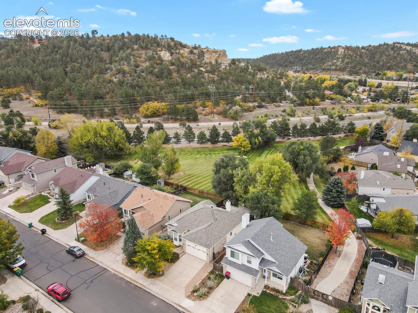 Aerial perspective showcasing a residential property with an attached two-car garage, concrete driveway, asphalt shingle roofing, and expansive green space featuring mature landscaping