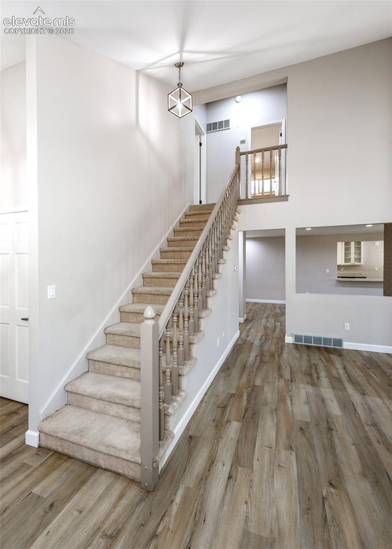 Open living space featuring wood-finish flooring, a carpeted staircase with wood banisters, and a geometric pendant light fixture