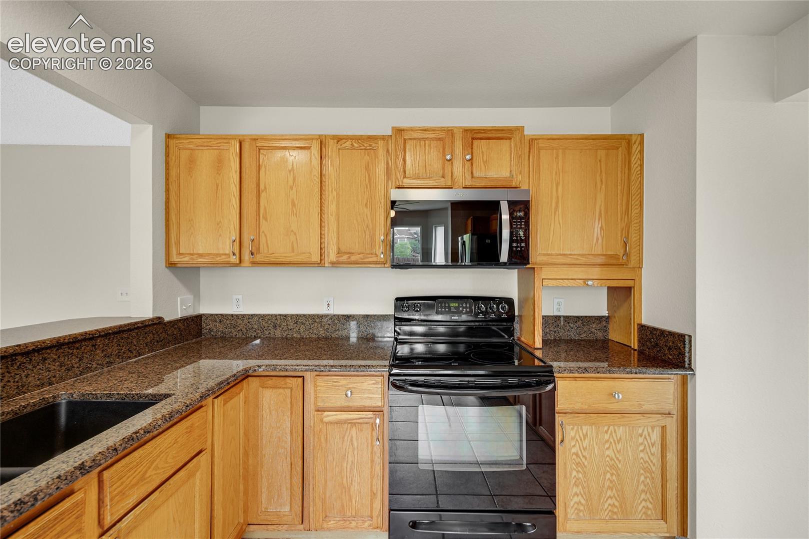 Kitchen featuring natural-finish wood cabinetry, speckled stone countertops, a dark-toned drop-in sink, and black appliances including a freestanding range and over-the-range microwave
