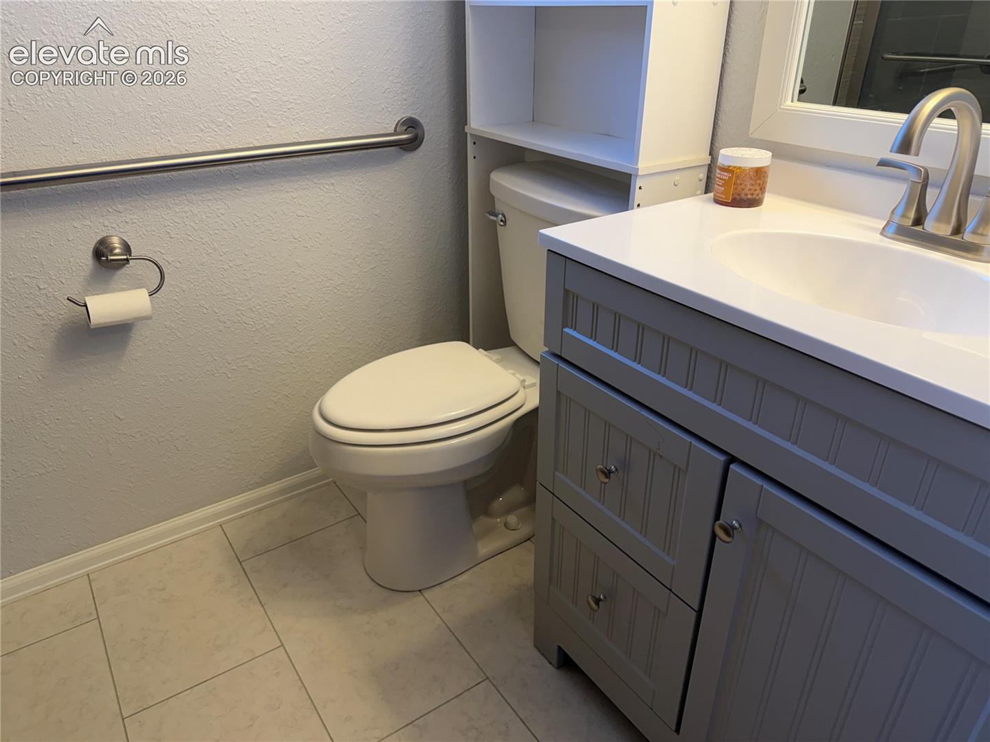 Updated bathroom in lower level with grey vanity cabinet featuring beadboard detailing, white countertop with integrated basin, brushed nickel hardware, and tile flooring