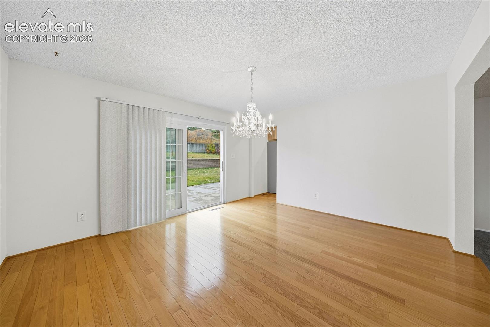 Living space featuring wood-finish flooring, a decorative crystal chandelier, and sliding glass doors with vertical blinds
