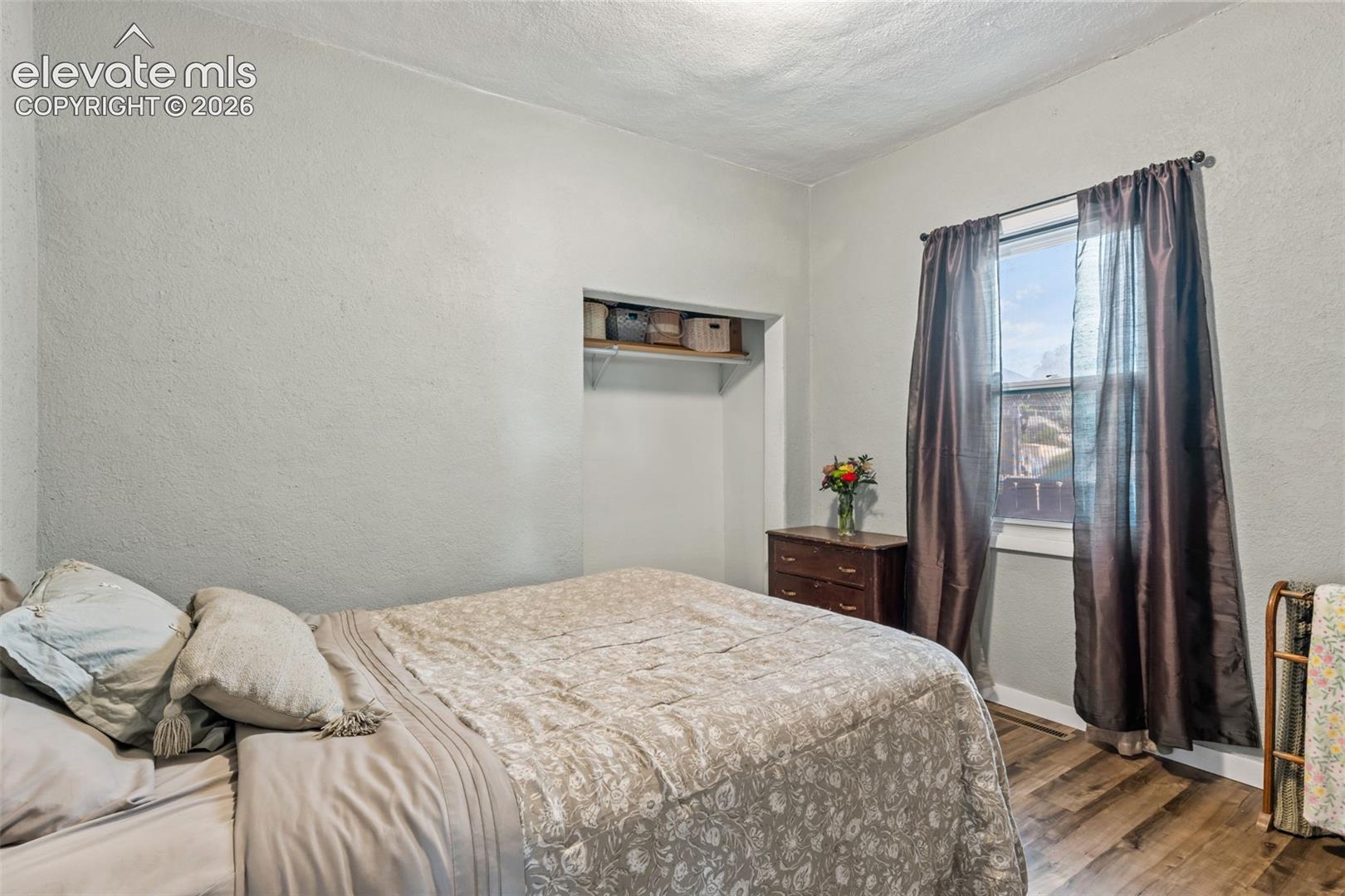 Room featuring wood-finish flooring, a built-in recessed shelving unit, and a window with a curtain rod