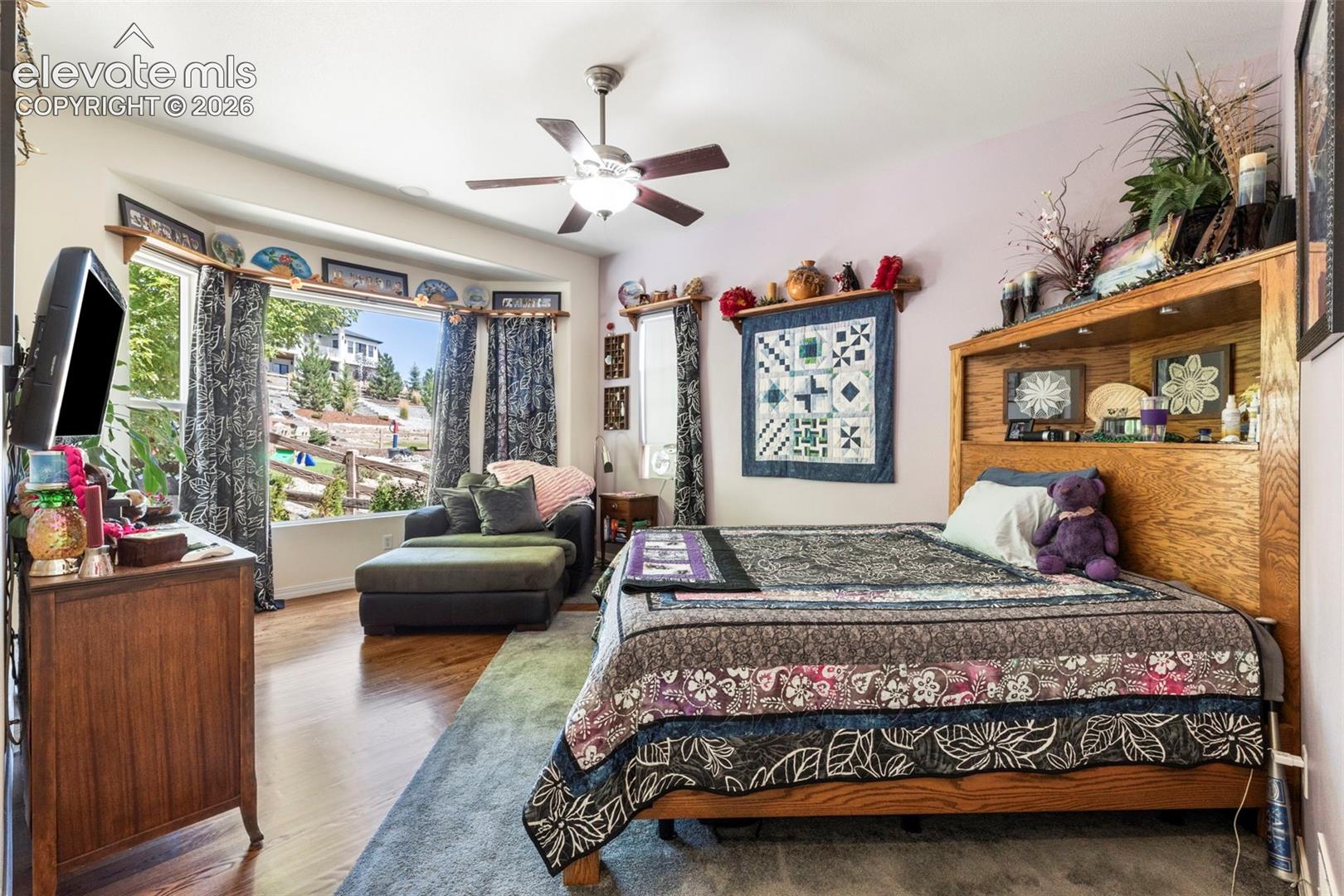Wood-finish flooring, ceiling fan, built-in headboard shelving, built-in window seating, and a bay window