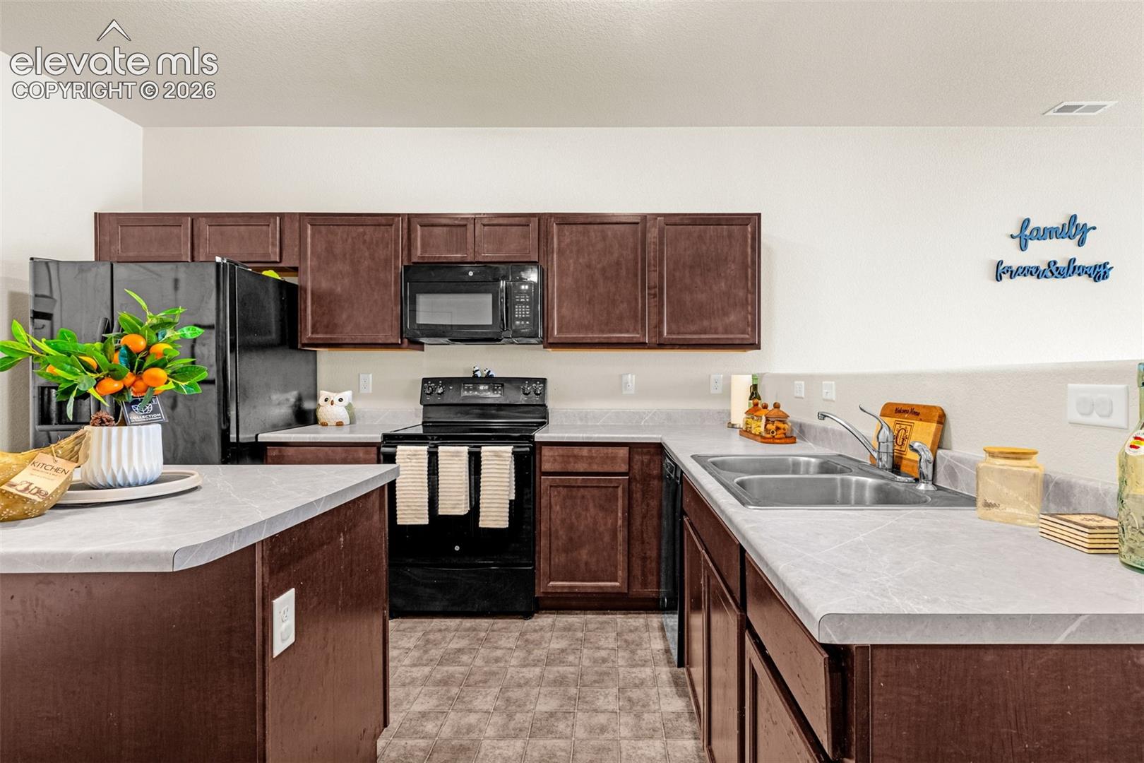 Kitchen featuring dark wood-finish cabinetry, light-toned countertops, and a full suite of black appliances, including a refrigerator, range, microwave, and dishwasher