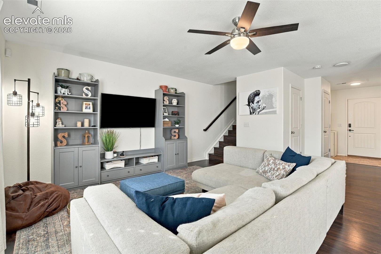 Integrated entertainment center with shelving, dark wood-finish flooring, staircase with dark wood handrail, and white paneled interior door