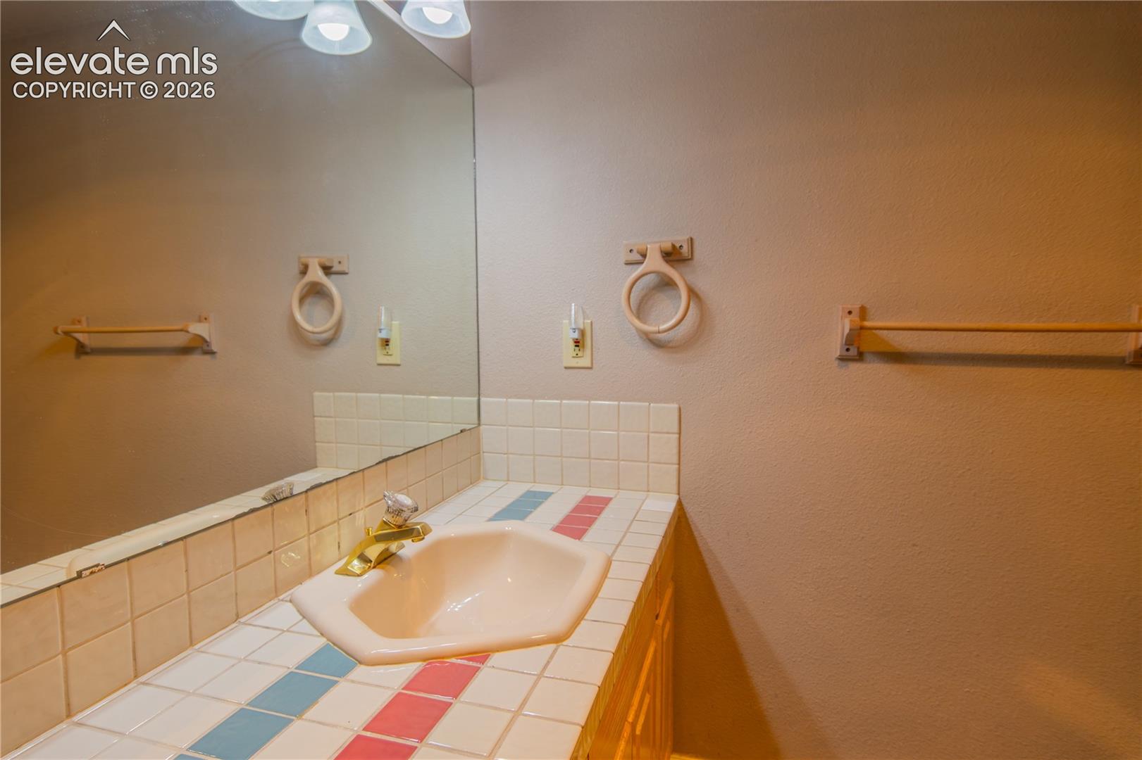 Vanity with a drop-in sink, tiled countertop, and a large wall-mounted mirror