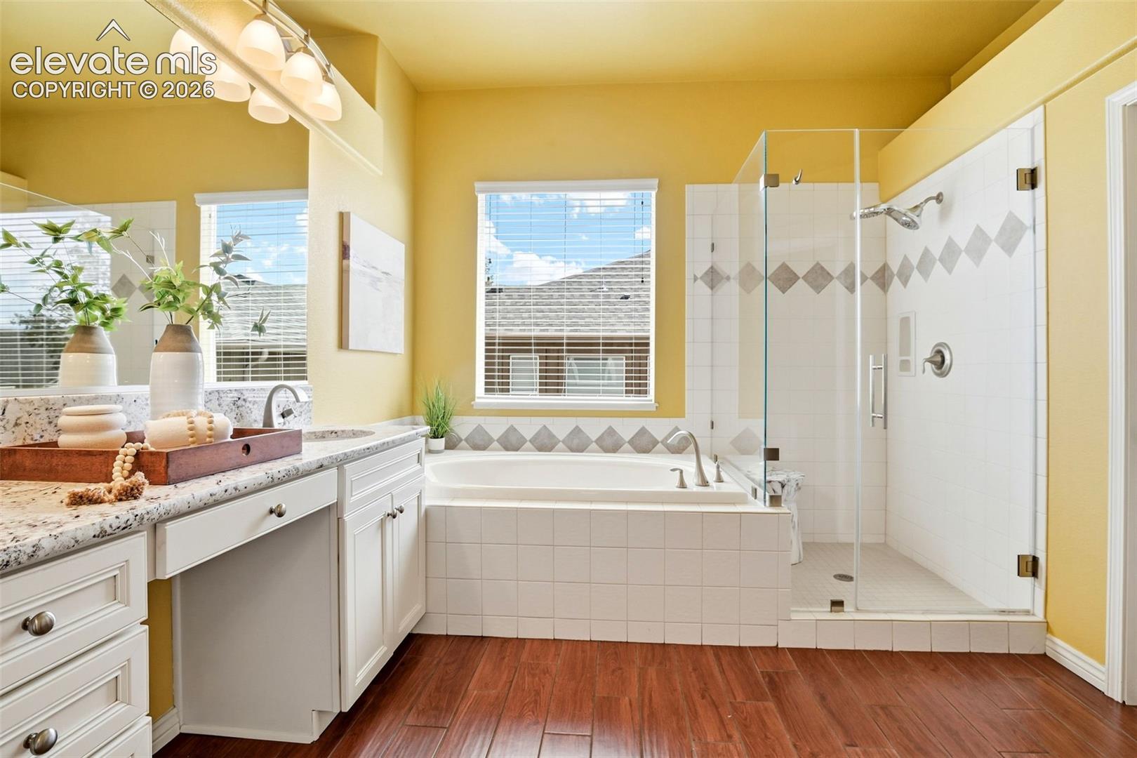 Bright and spacious primary bathroom!  Deep soaking tub, glass shower with stylish dual shower head, finished with durable wood look porcelain tile, steps from a large walk-in closet.